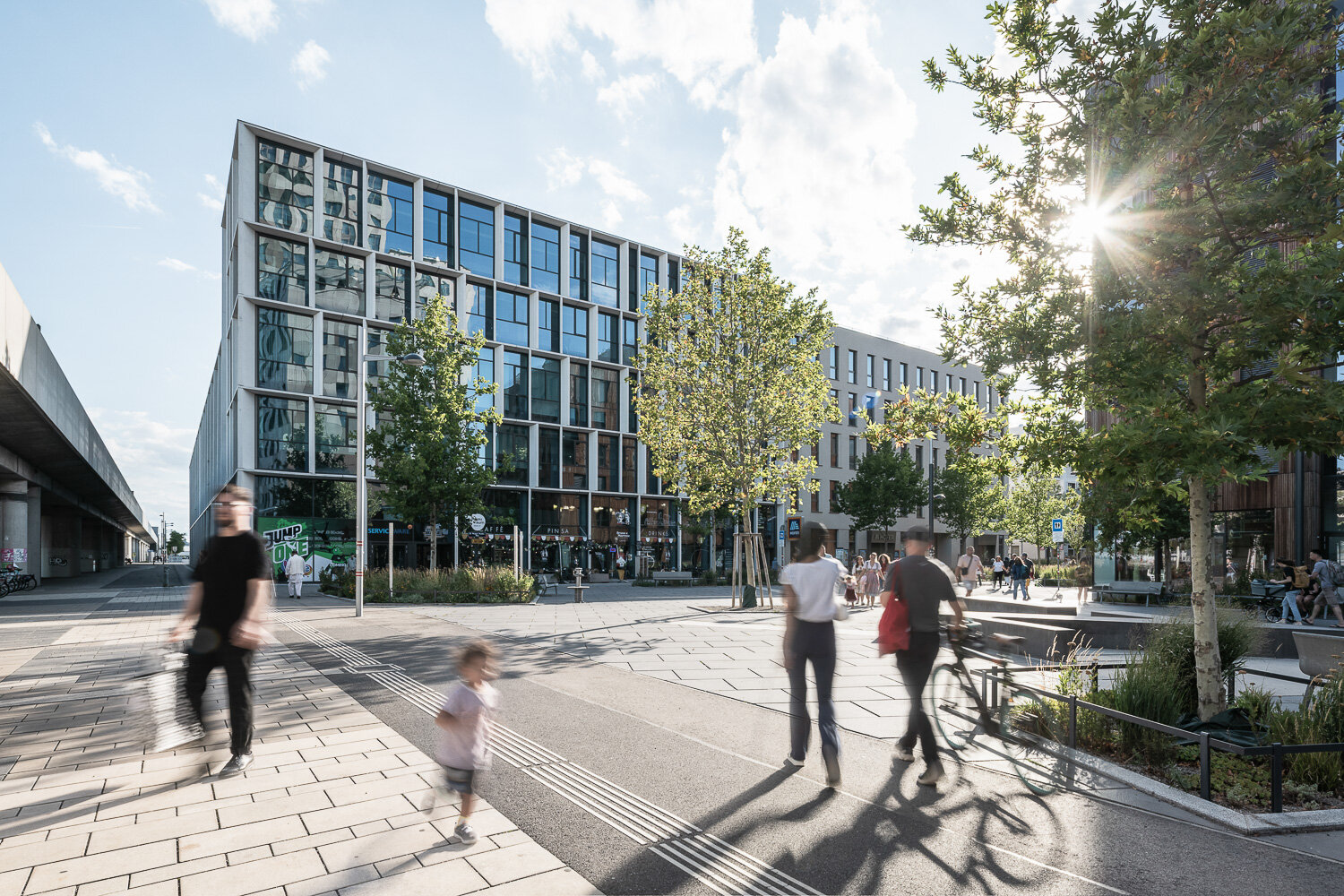 Seehub direkt an der U-Bahn modernes Bürogebäude mit großen Fensterfronten auf einem Platz mit Menschen und großen Bäumen