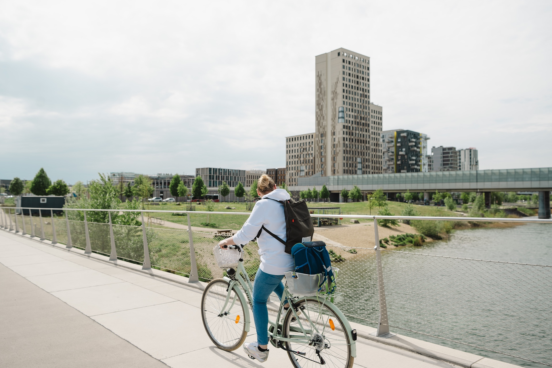 Radfahren in die Seestadt Frau auf einem Rad, die auf der Straße in die Seestadt fährt im Vordergrund, Seestadt mit HoHo Wien im Hintergrund
