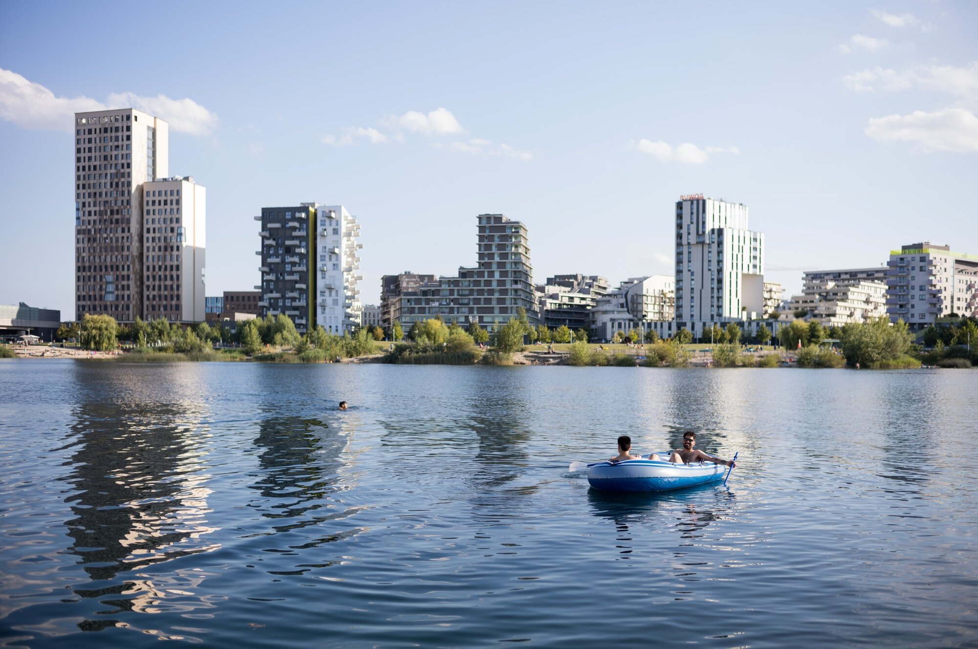 Schlauchboot und Schwimmer im asperner See mit Seepark und der Skyline vom Seeparkquartier
