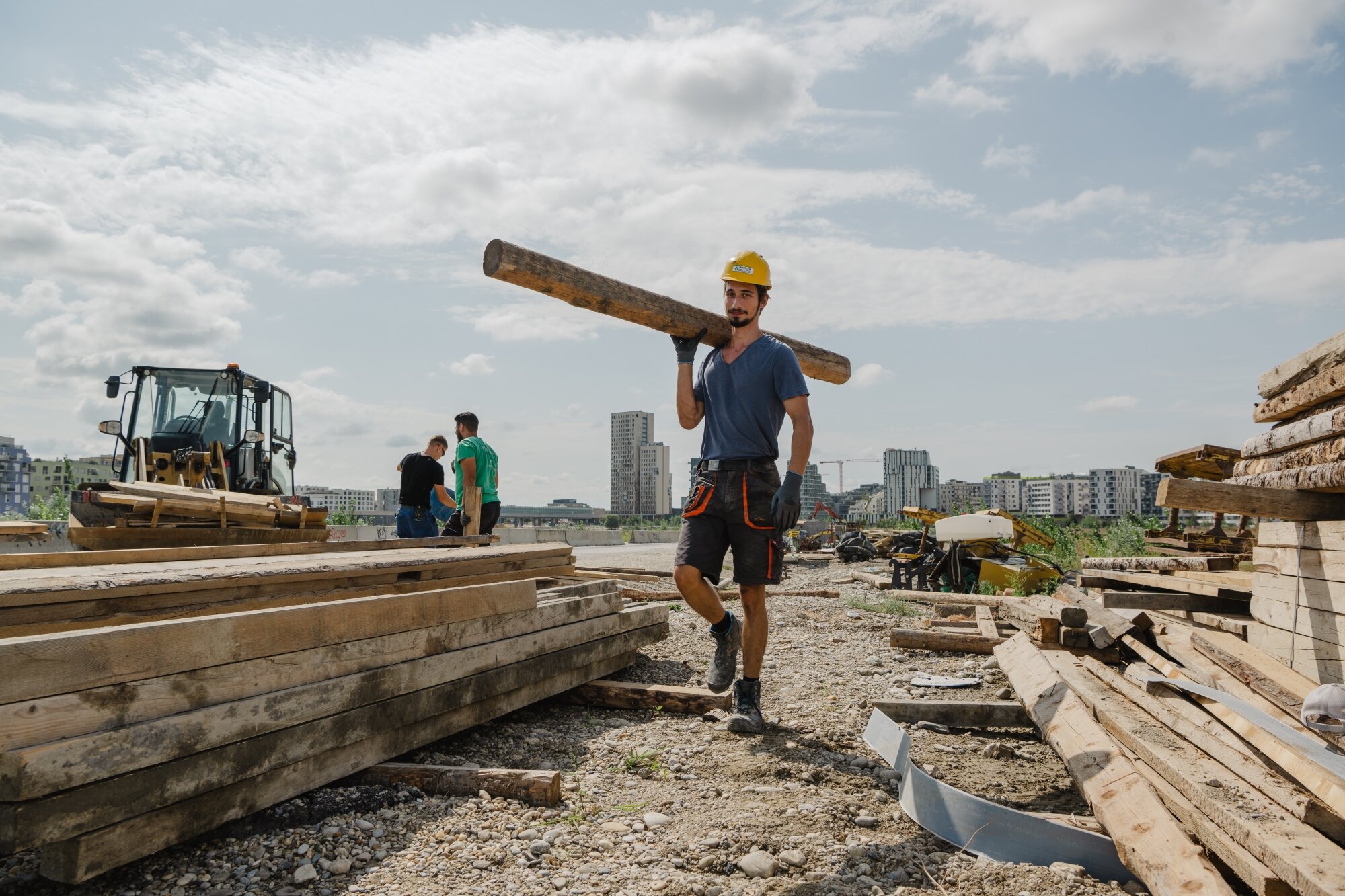 Bauarbeiter trägt Holz auf einer Baustelle vor einer modernen Skyline
