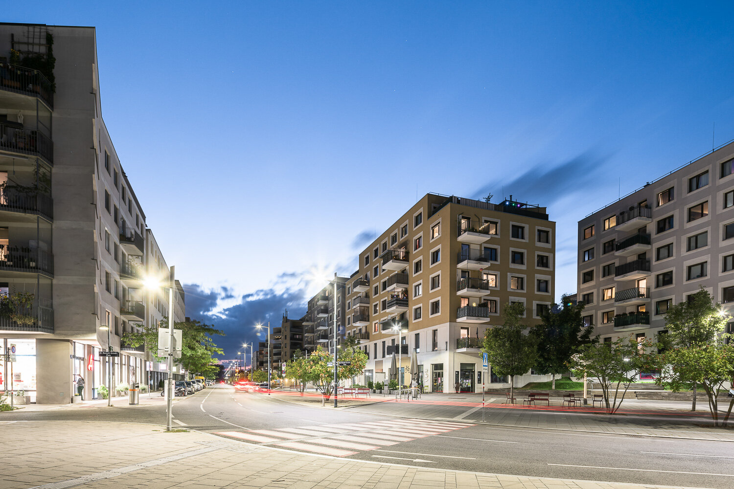Straße mit Bäumen und modernen Gebäuden in der Dämmerung