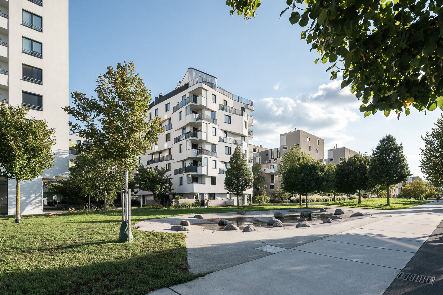 Wasserspielplatz in einem Park mit Bäumen vor Wohnhäusern mit Balkonen