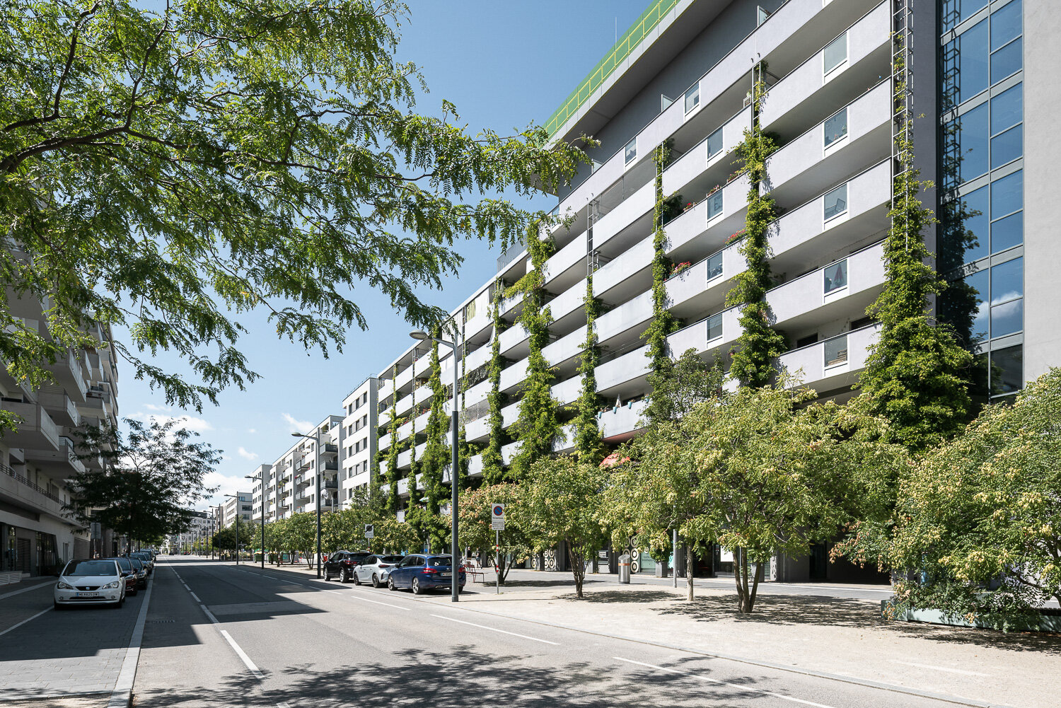 begrünte Fassade eines Hauses mit vielen Balkonen an einer Allee