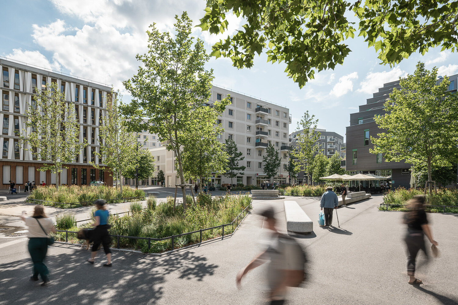 Menschen auf einem Platz mit Bäumen und Grüninseln und modernen hochwertigen Gebäuden