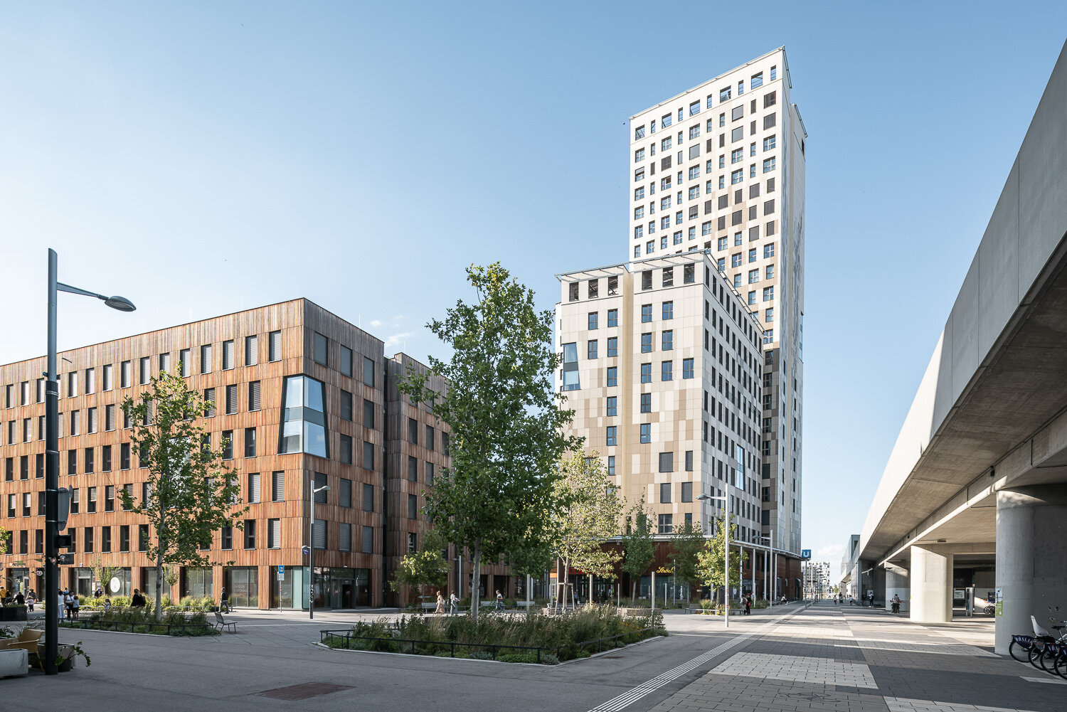 Hochhaus und Holzhaus mit Büros und Hotel auf begrüntem Platz an der U-Bahn