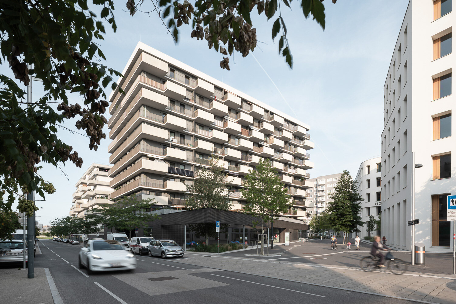 reduzierter Autoverkehr in der Seestadt Straße mit fahrenden und parkenden Autos, modernen Gebäuden und einem Platz mit Bäumen