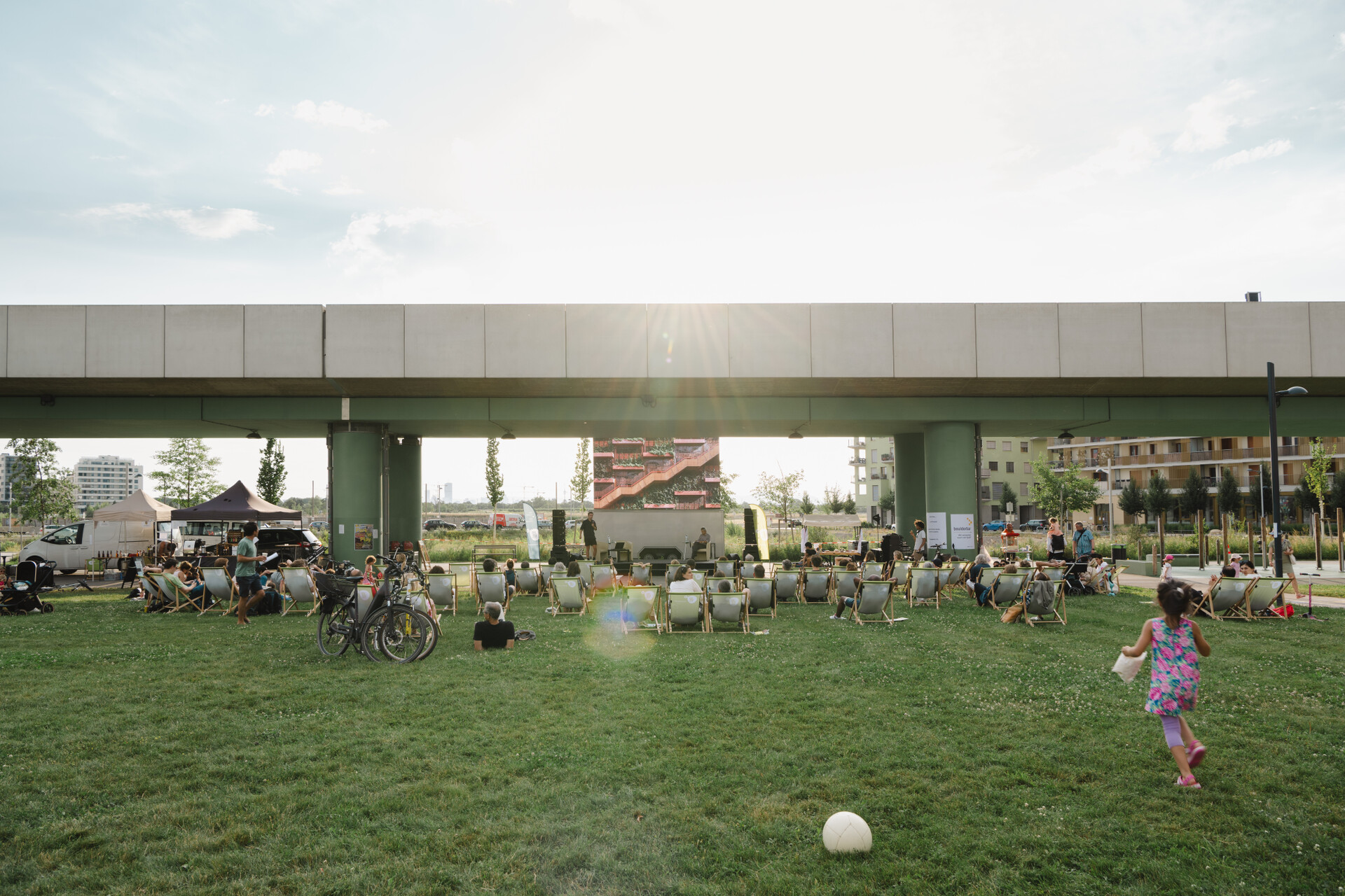 Der Elinor-Ostrom-Park bietet Sport und Spiel für alle Generationen. Spielende Personen und Kinder auf einer Wiese, im Hintergrund U-Bahnbauwerk.