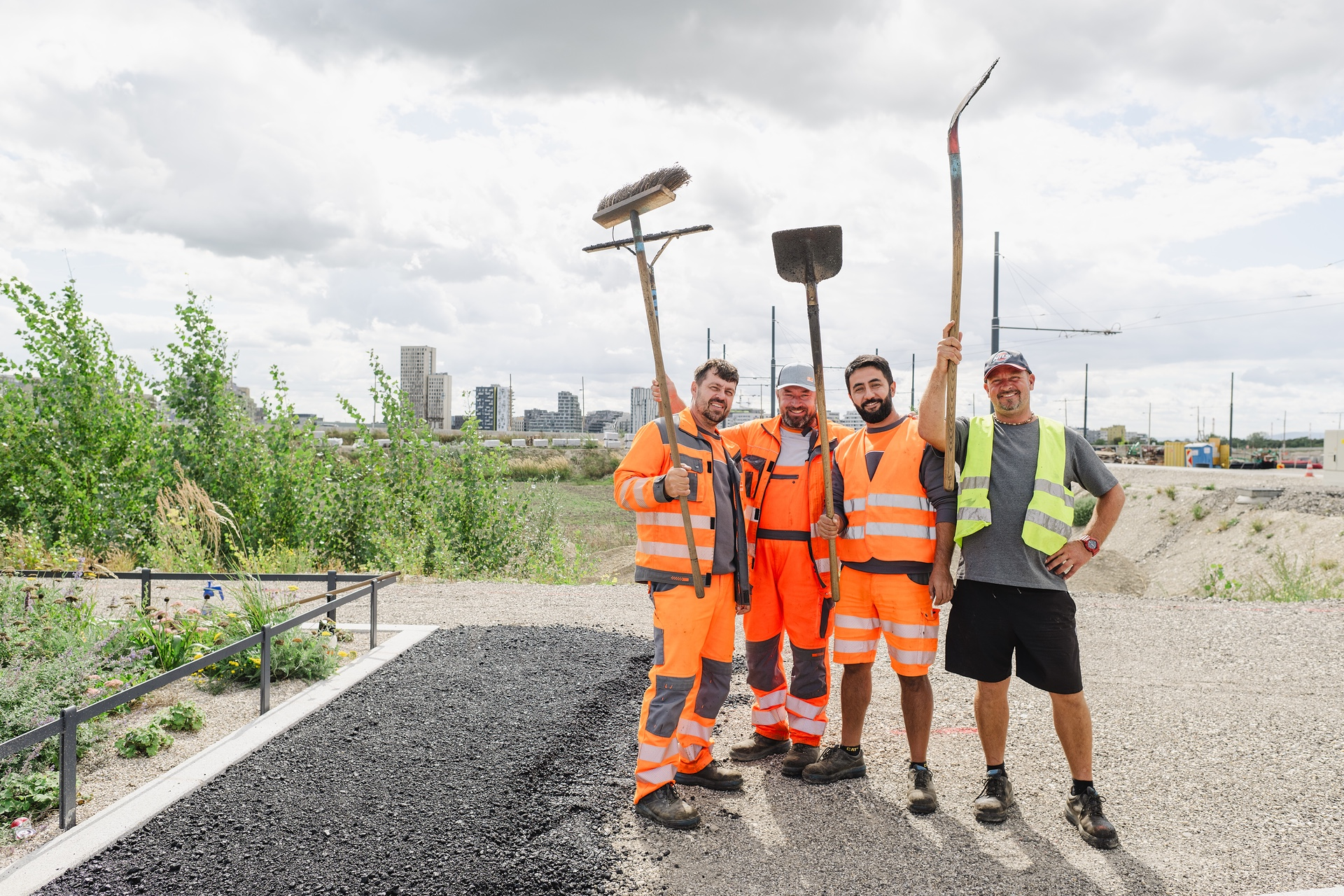 Vier männliche Personen in Arbeitsmontur vor der Skyline der Seestadt. 