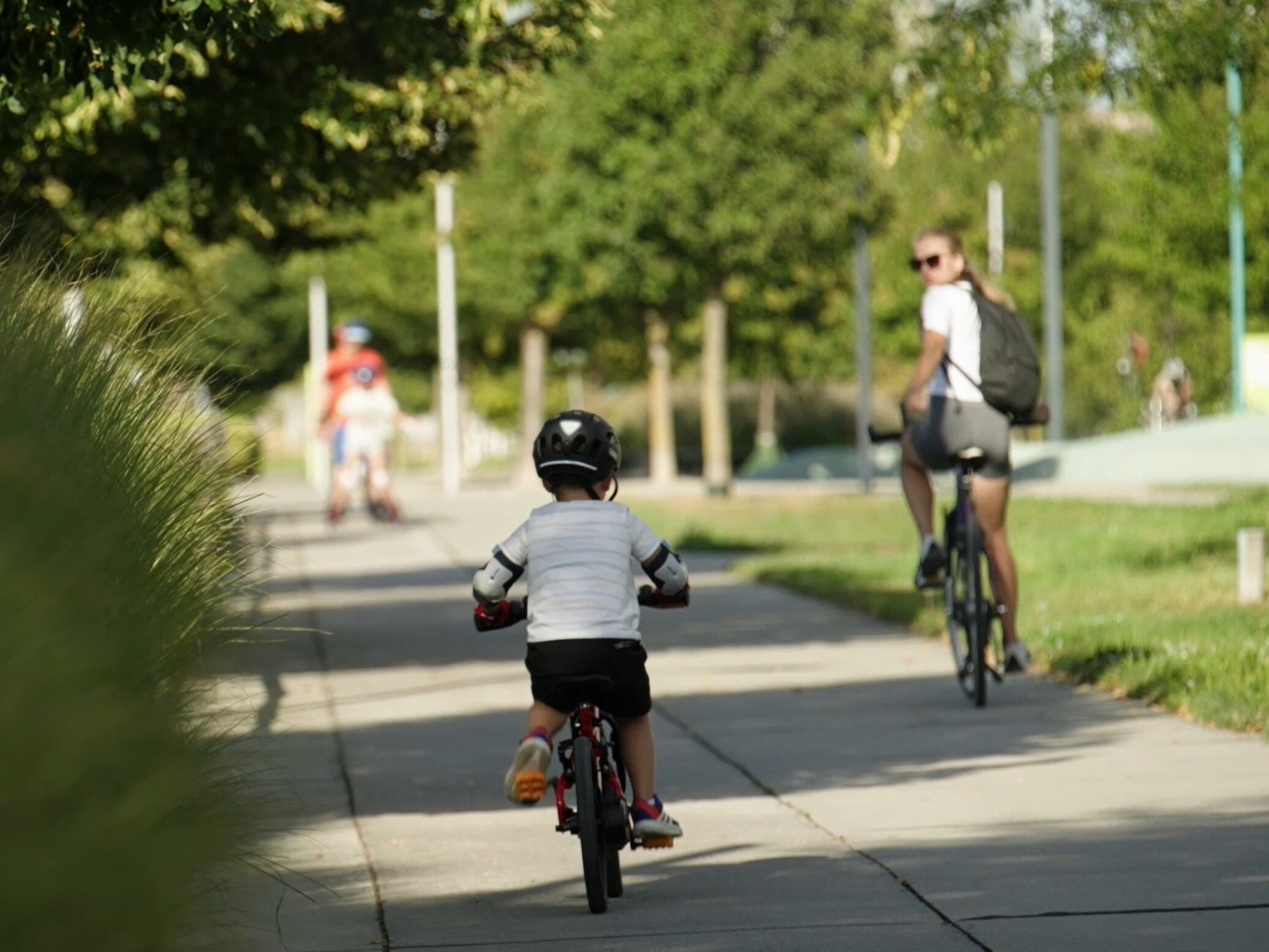 Mutter mit kleinem Kind mit Helm, beide auf einem Fahrrad auf einem Weg, der durch Natur führt
