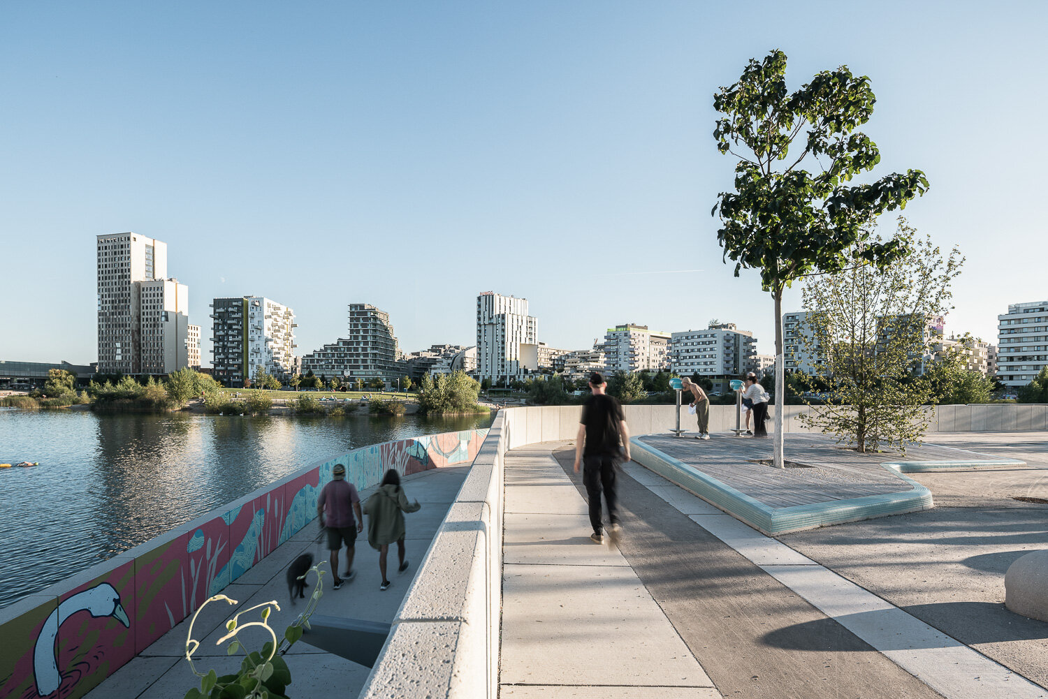 Menschen spazieren am Nordufer des Sees in der Seestadt mit Blick auf die Skyline des Seeparkquartiers