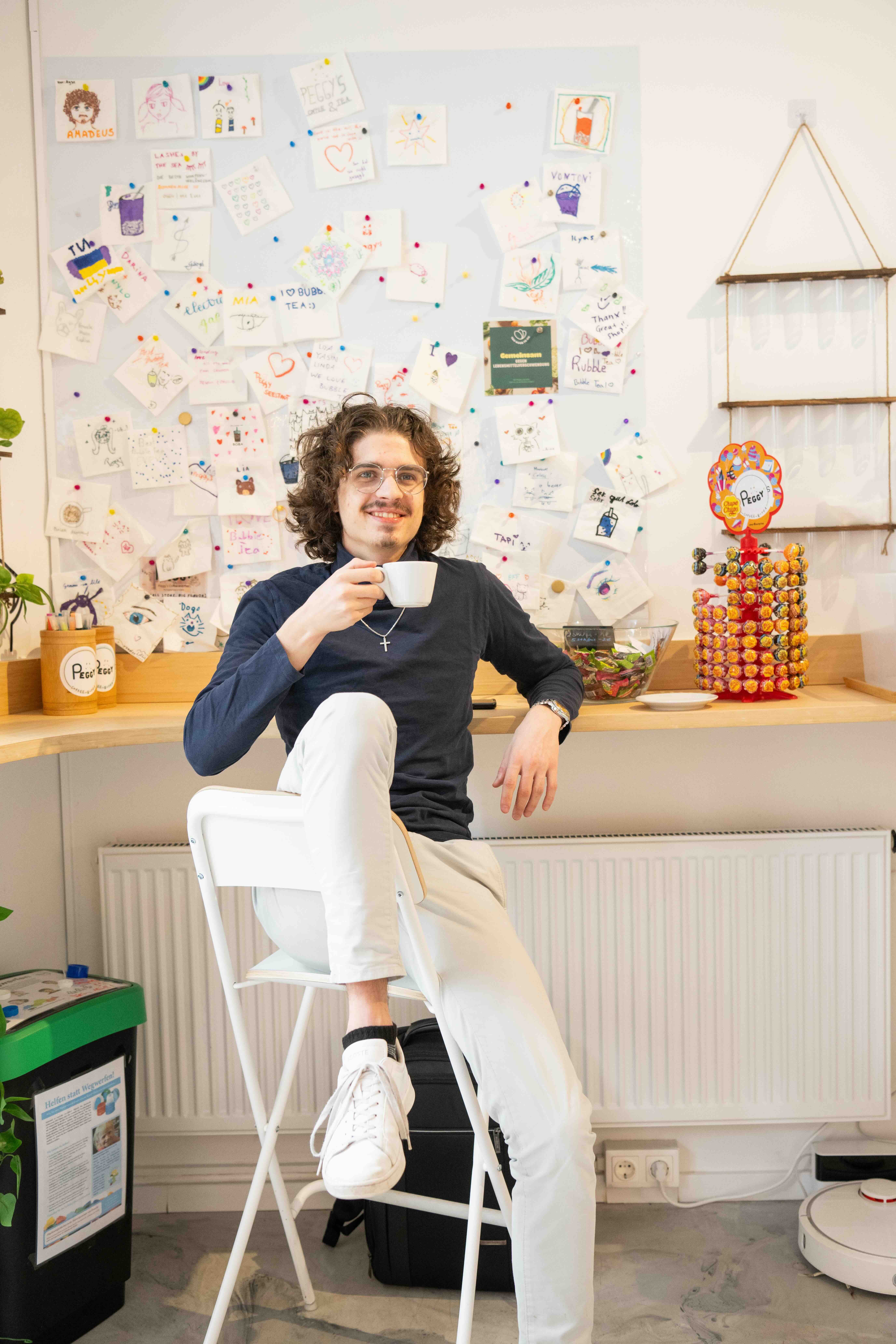 Mann sitzt auf einem Stuhl mit einer Tasse Kaffee in der Hand