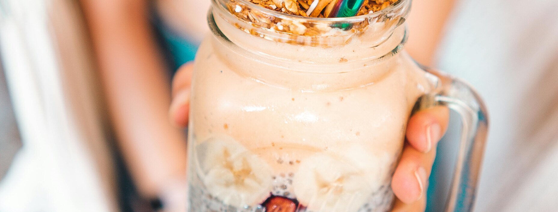 Hand mit Glas, in dem ein schaumiger Smoothie mit Strohhalm ist