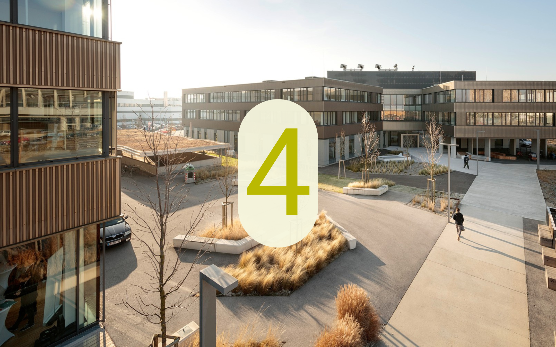 Moderner Gewerbe- und Bürostandort in der Seestadt mit begrünten Außenflächen und der eingeblendeten Zahl 4.