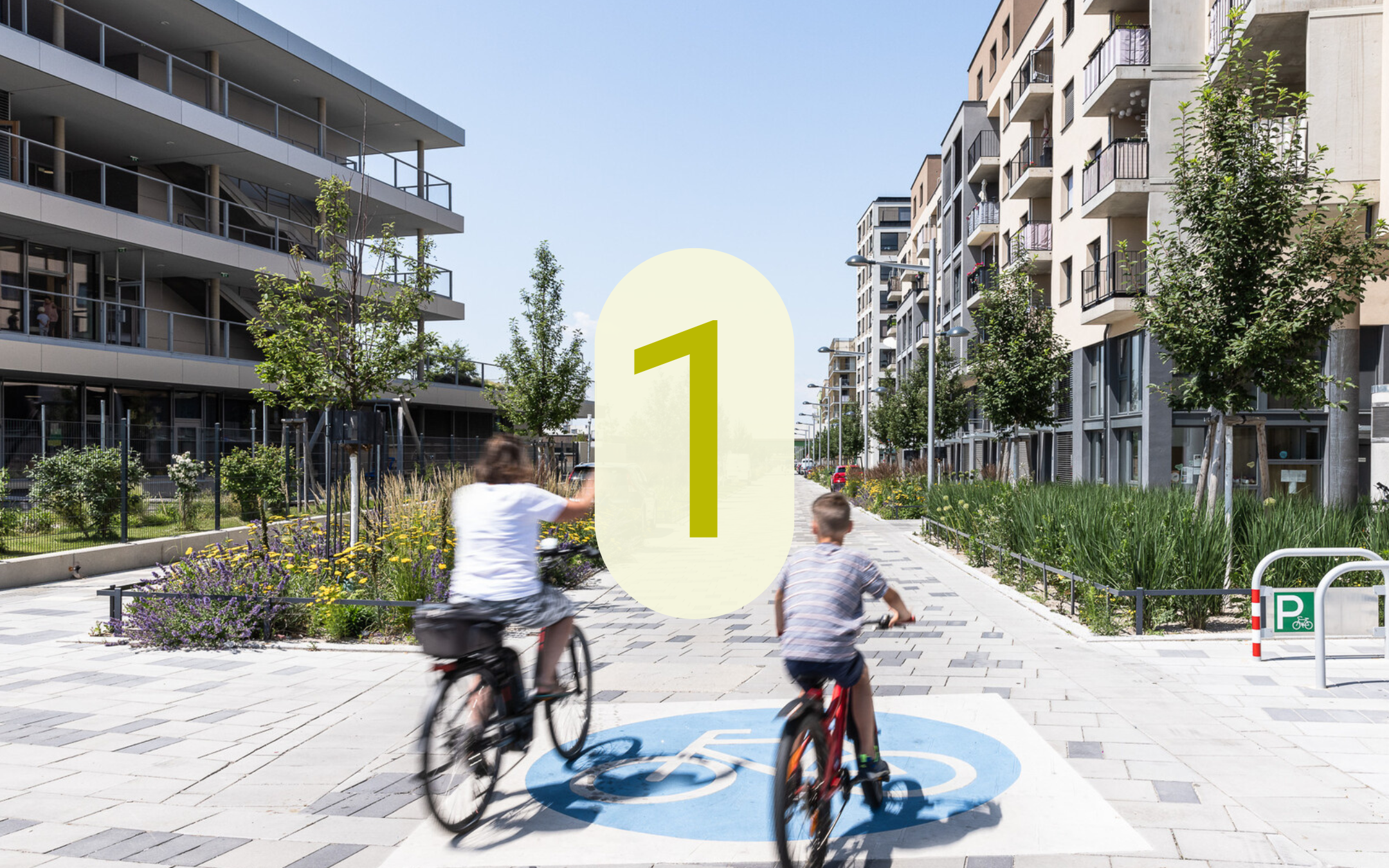 Breiter begrünter Rad- und Fußweg zwischen Wohngebäuden in der Seestadt mit zwei Radfahrenden und der eingeblendeten Zahl 1.