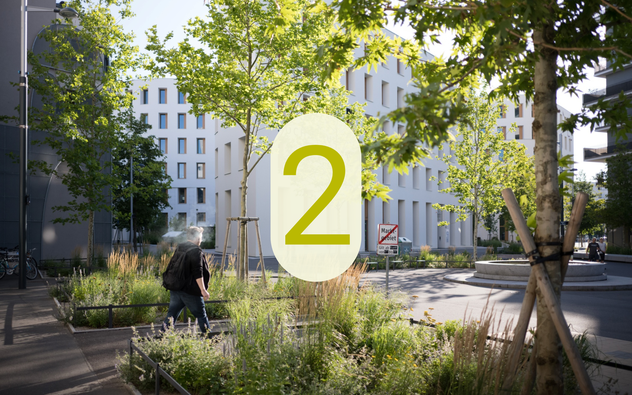 Begrünter Straßenraum in der Seestadt zwischen modernen Wohngebäuden mit einem Fußgänger und der eingeblendeten Zahl 2.