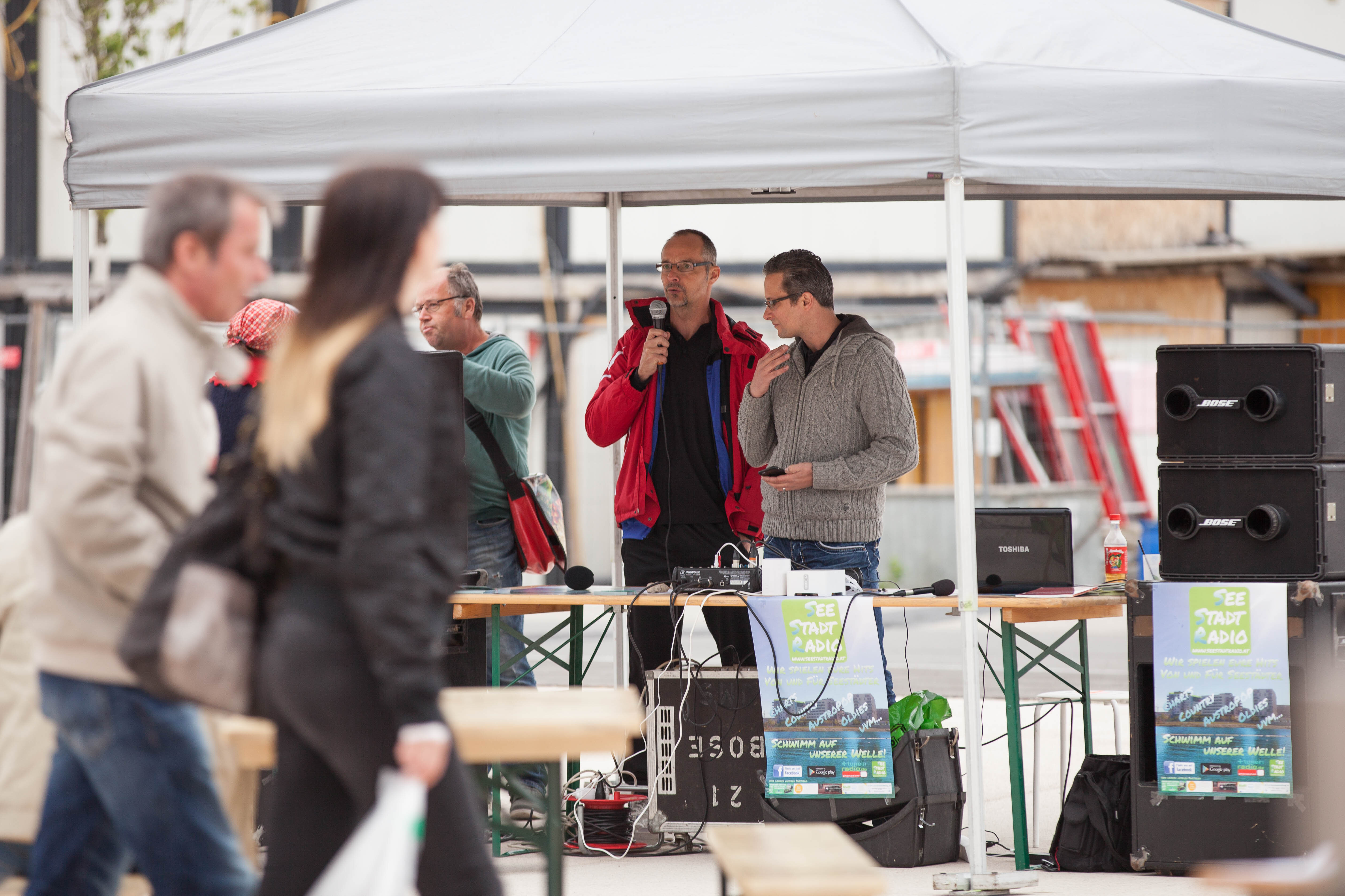 Zelt des Seestadtradios im Rahmen der Verantsaltung "Marktplatz der Initiativen". Unter dem Zelt sind zwei Mitarbeiter zu sehen. Jörg, der Seestadtreporter führt ein Interview. 