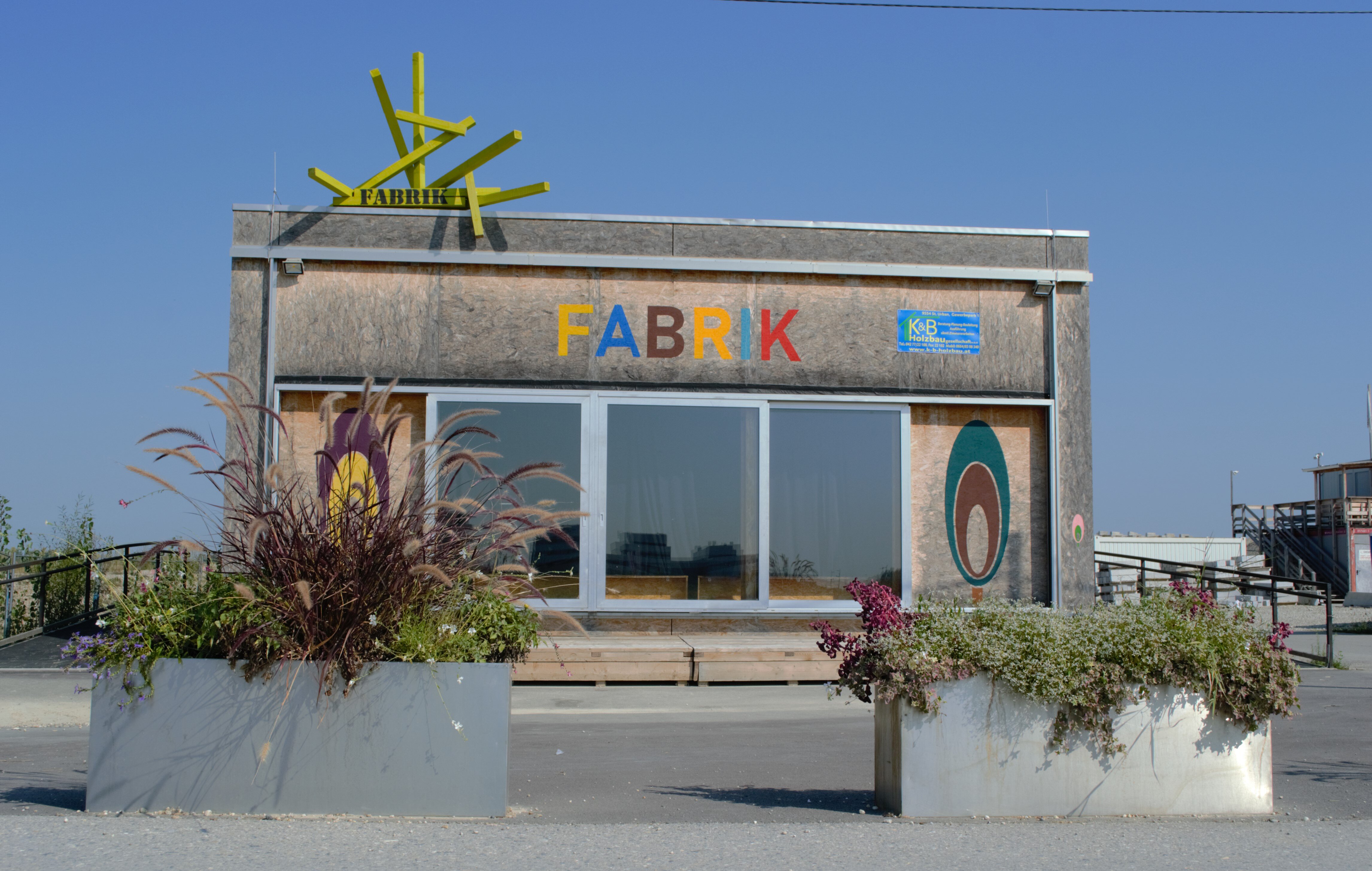 Veranstaltungshalle von außen mit Holzfassade und Aufschrift FABRIK