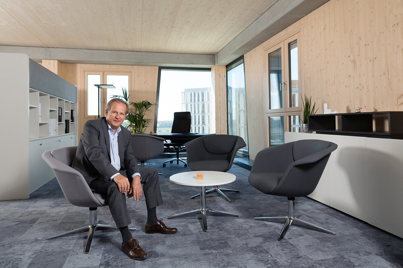 Investor und Visionär Günter Kerbler auf einem Stuhl sitzend, HoHo Wien Büro mit Holzoptik im Hintergrund.
