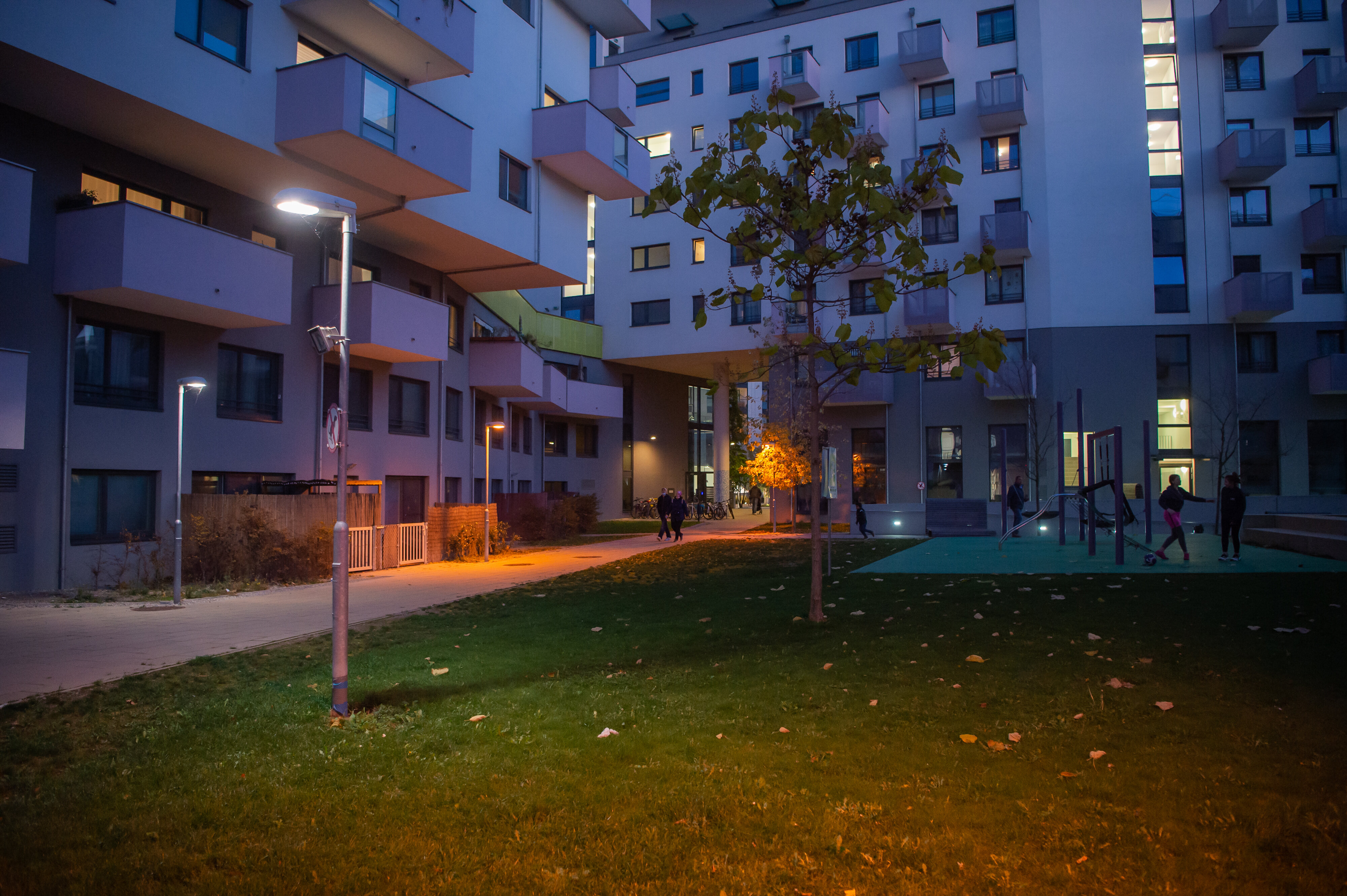 Gehweg in einer Wohnsiedlung mit guter Beleuchtung und mit Spaziergängern. 