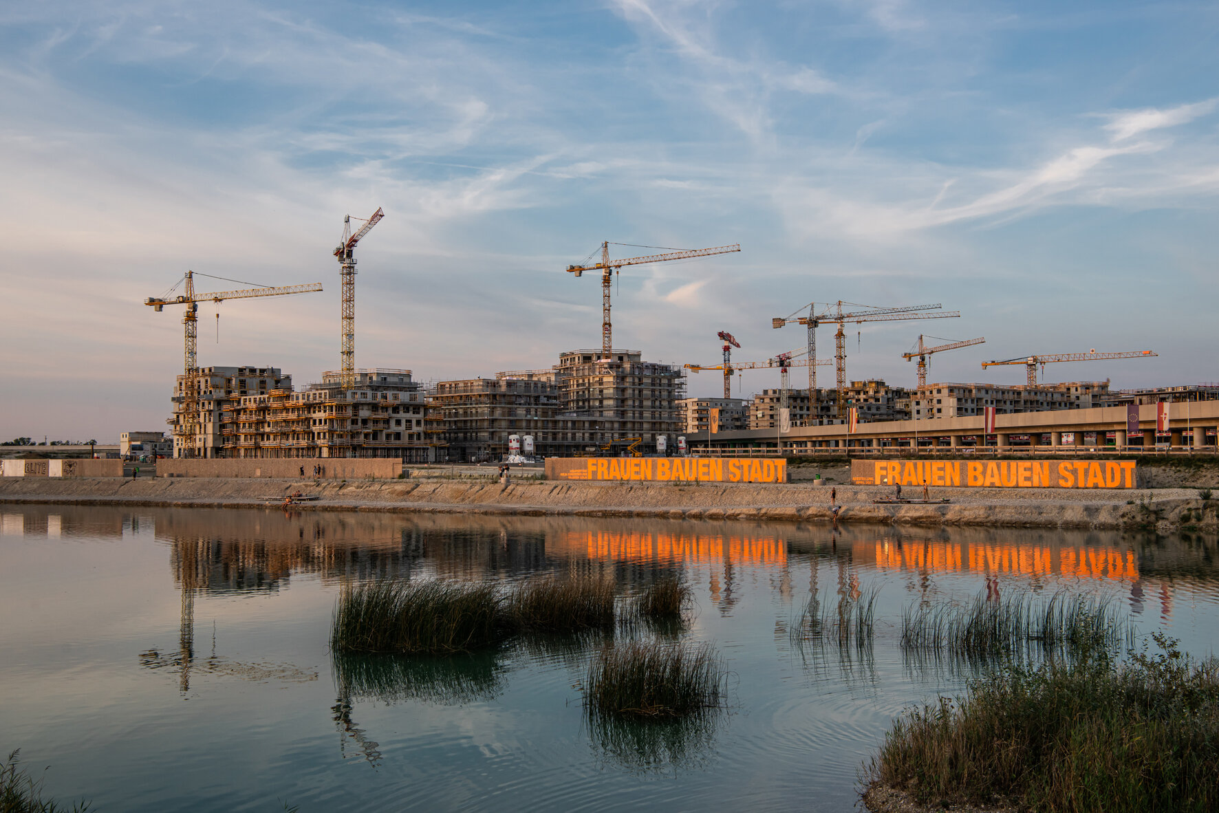 Aufschrift "Frauen Bauen Stadt" auf Bauzaun, dahinter Baustelle. Abendstimmung. 