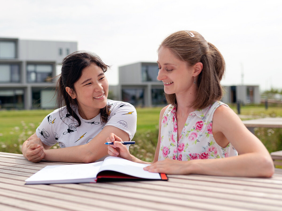 Zwei junge Frauen sitzen auf einer Parkbank und unterhalten sich.