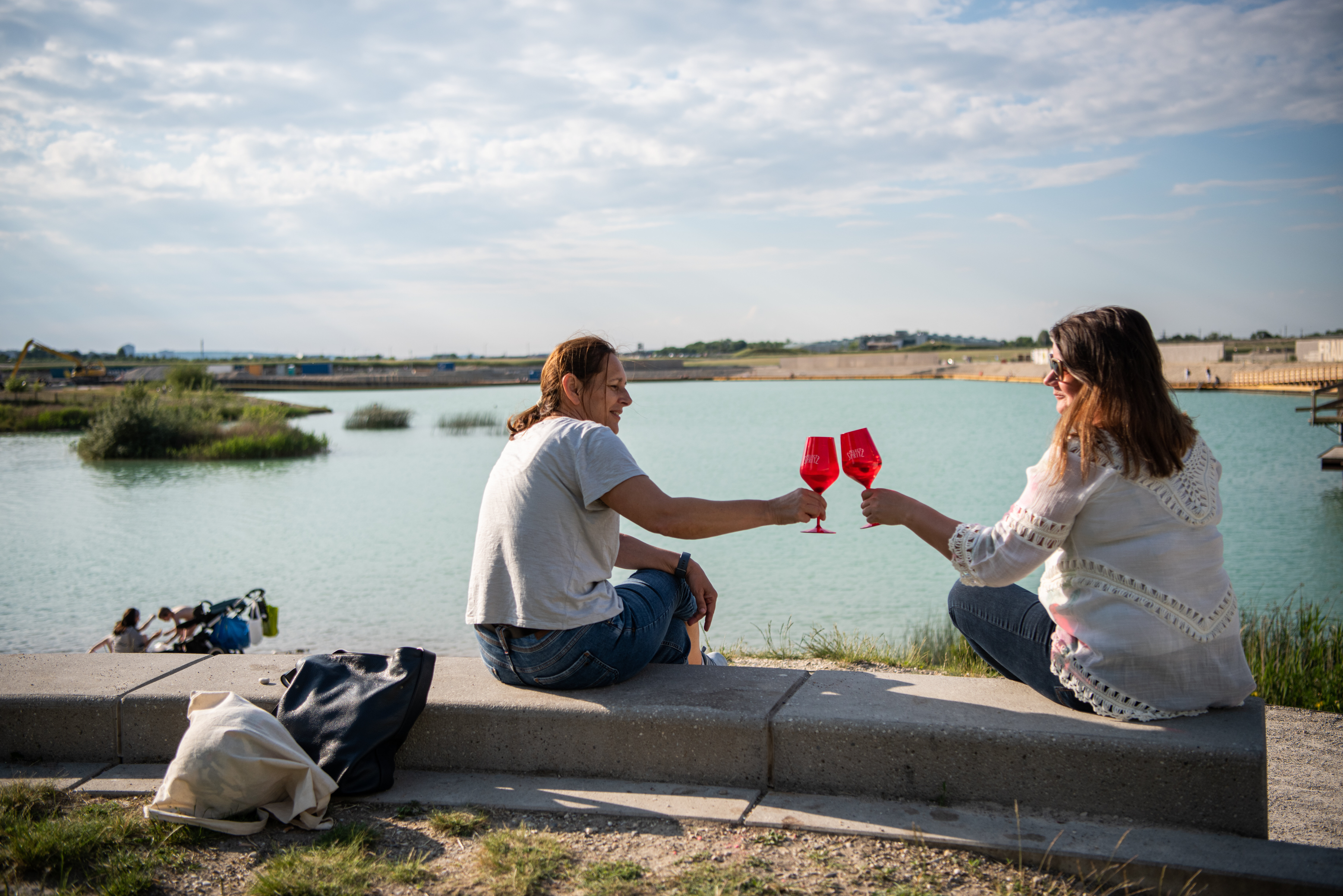 Zwei Frauen, die mit Gläsern anstoßen, im Hintergrund See. 