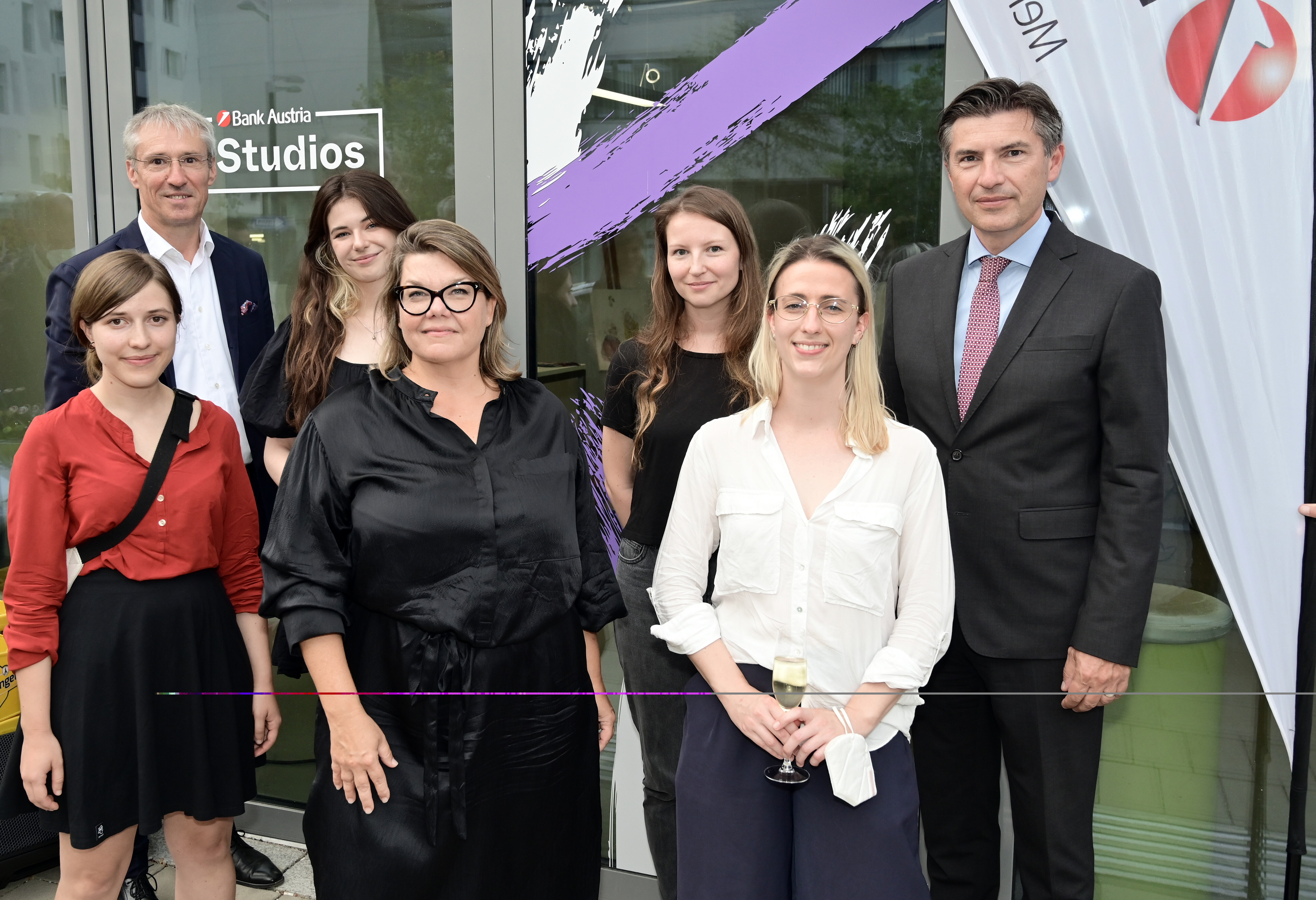 Sieben Personen vor einem modernen Eingang. 