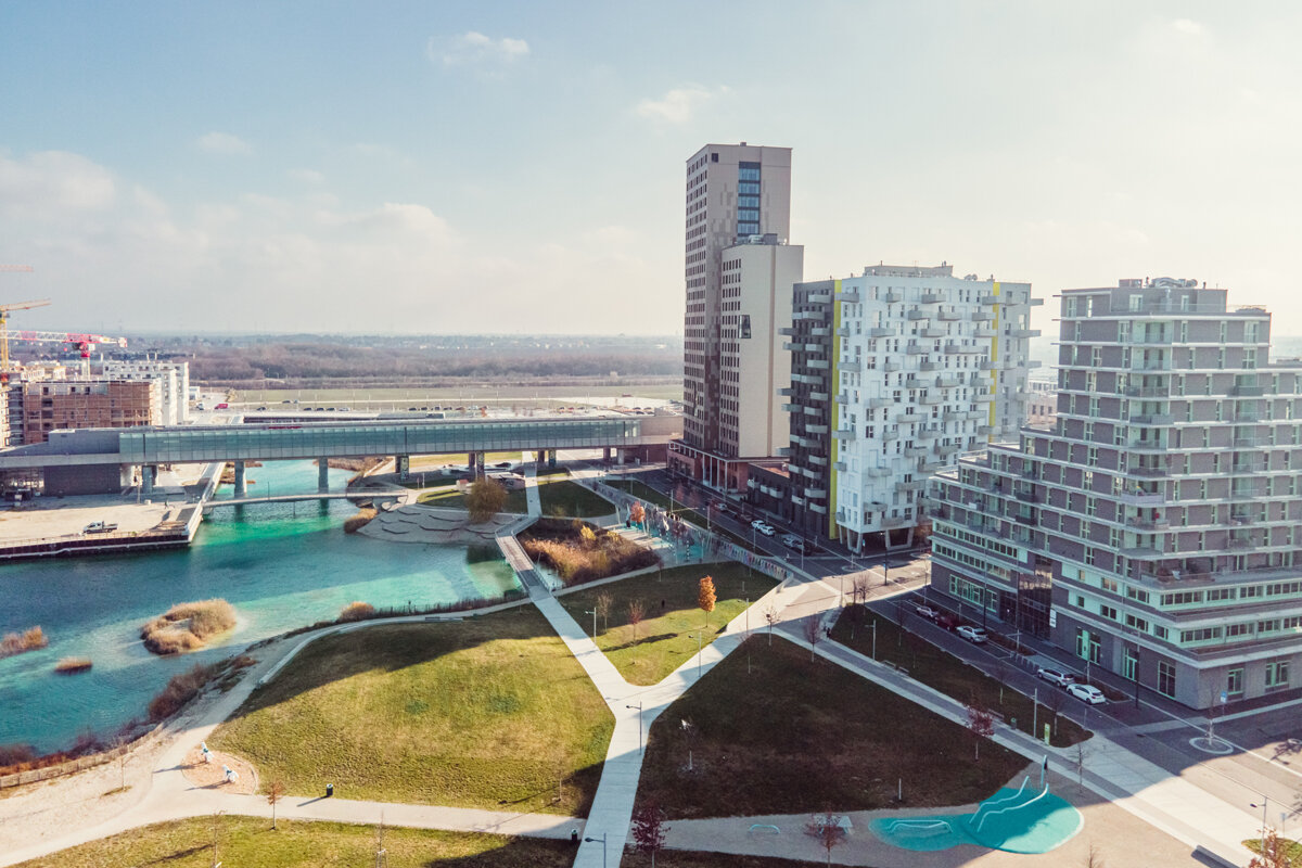 Ansicht von Westen über den Seepark, im Hintergrund HoHo Wien, U-Bahn und der türkisblaue See. 