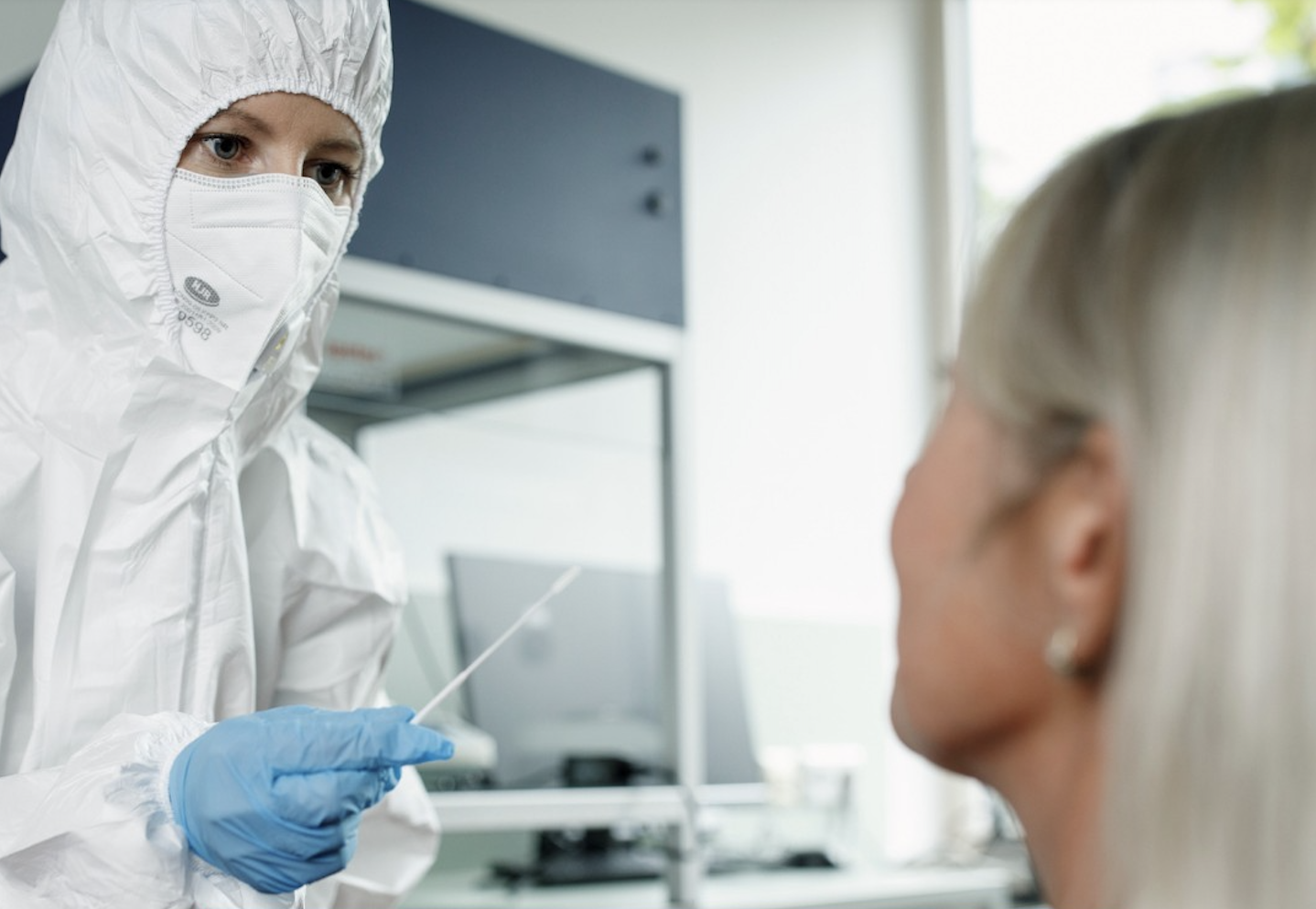 Person in Schuutzkleidung mit Coronateststäbchen in der Hand