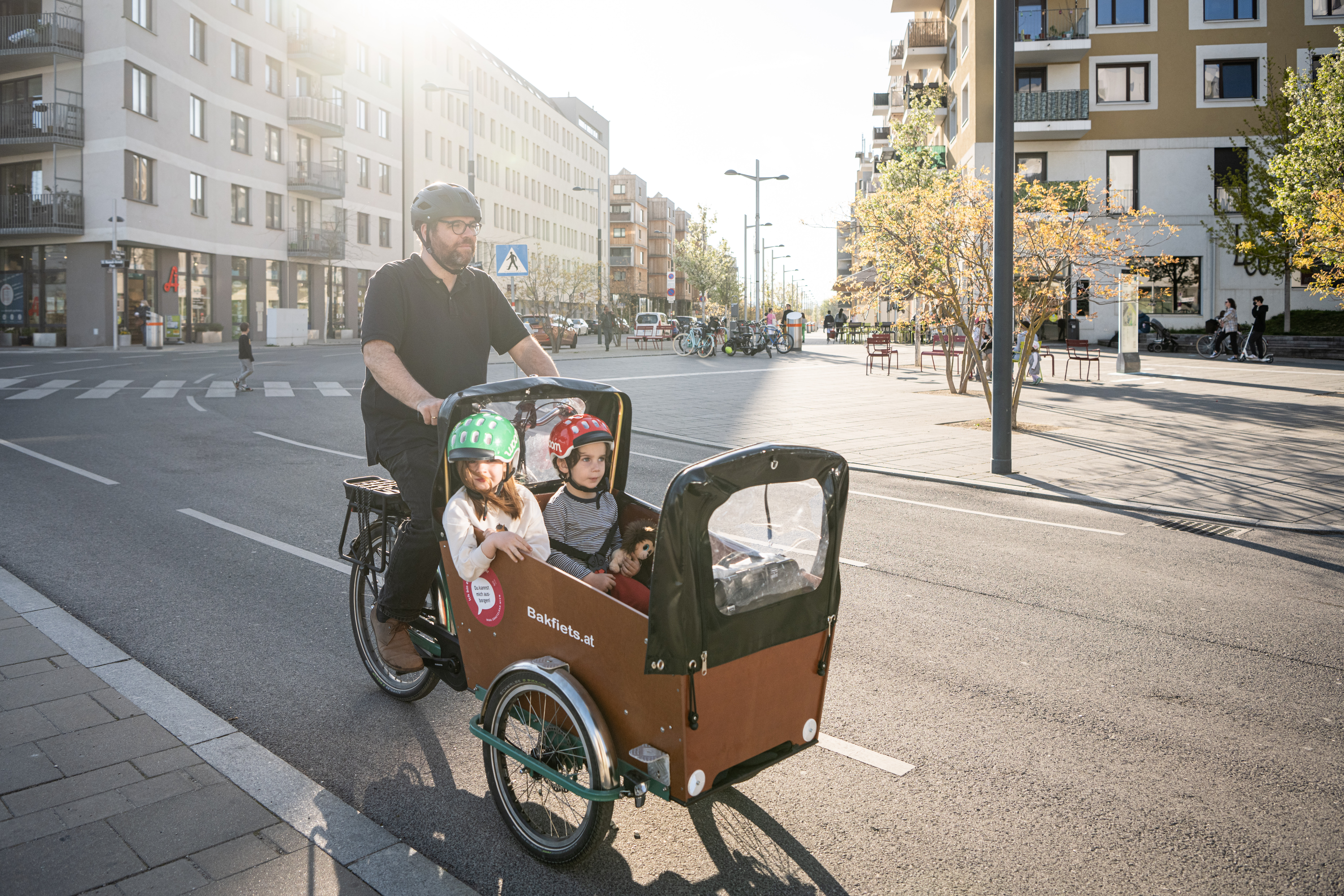 Mann fährt mit neuem Lastenrad, zwei Kinder sitzen vorne