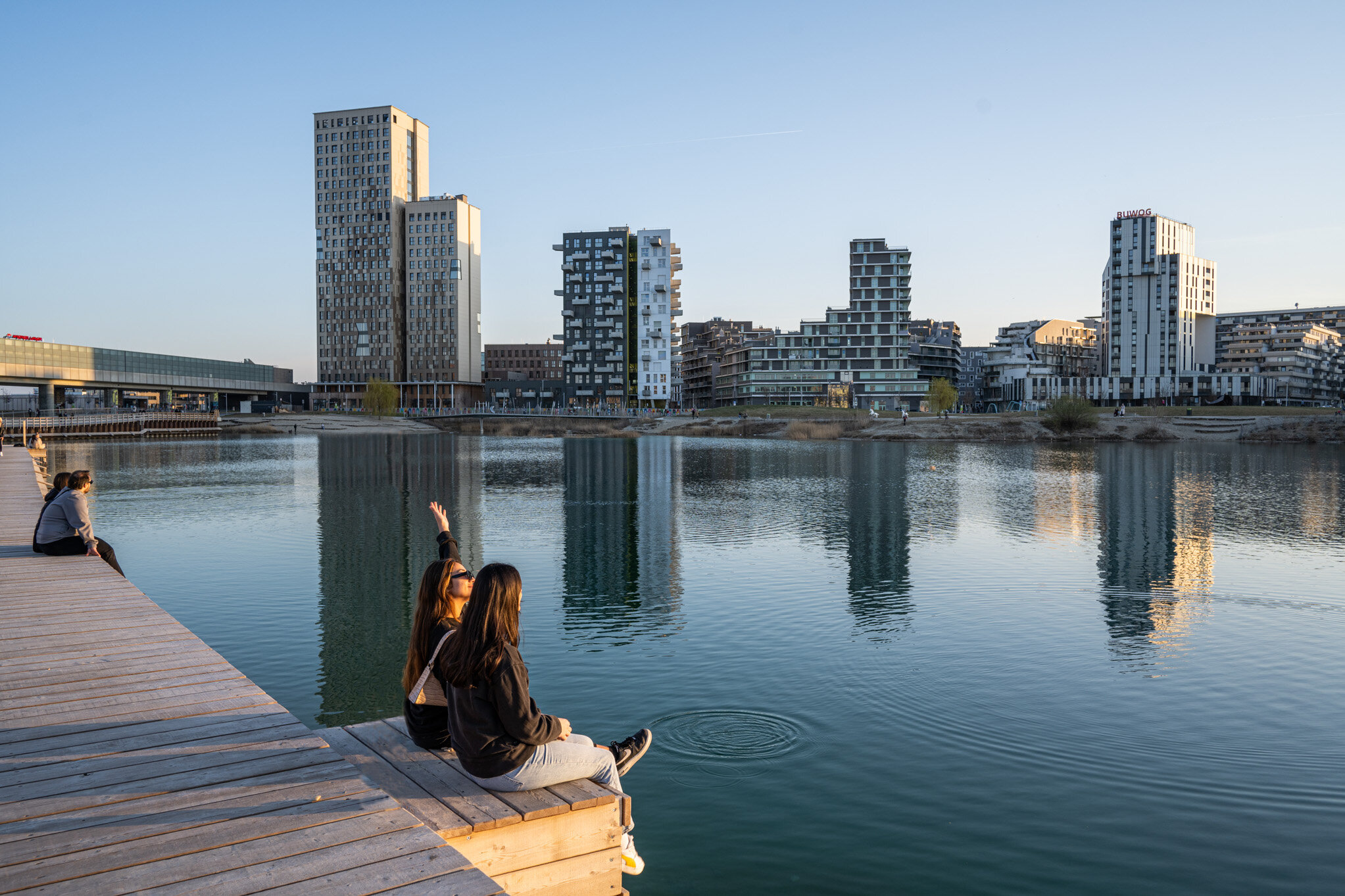 Menschen sitzen auf Steg beim See mit Blick Richtung Seeparkquartier