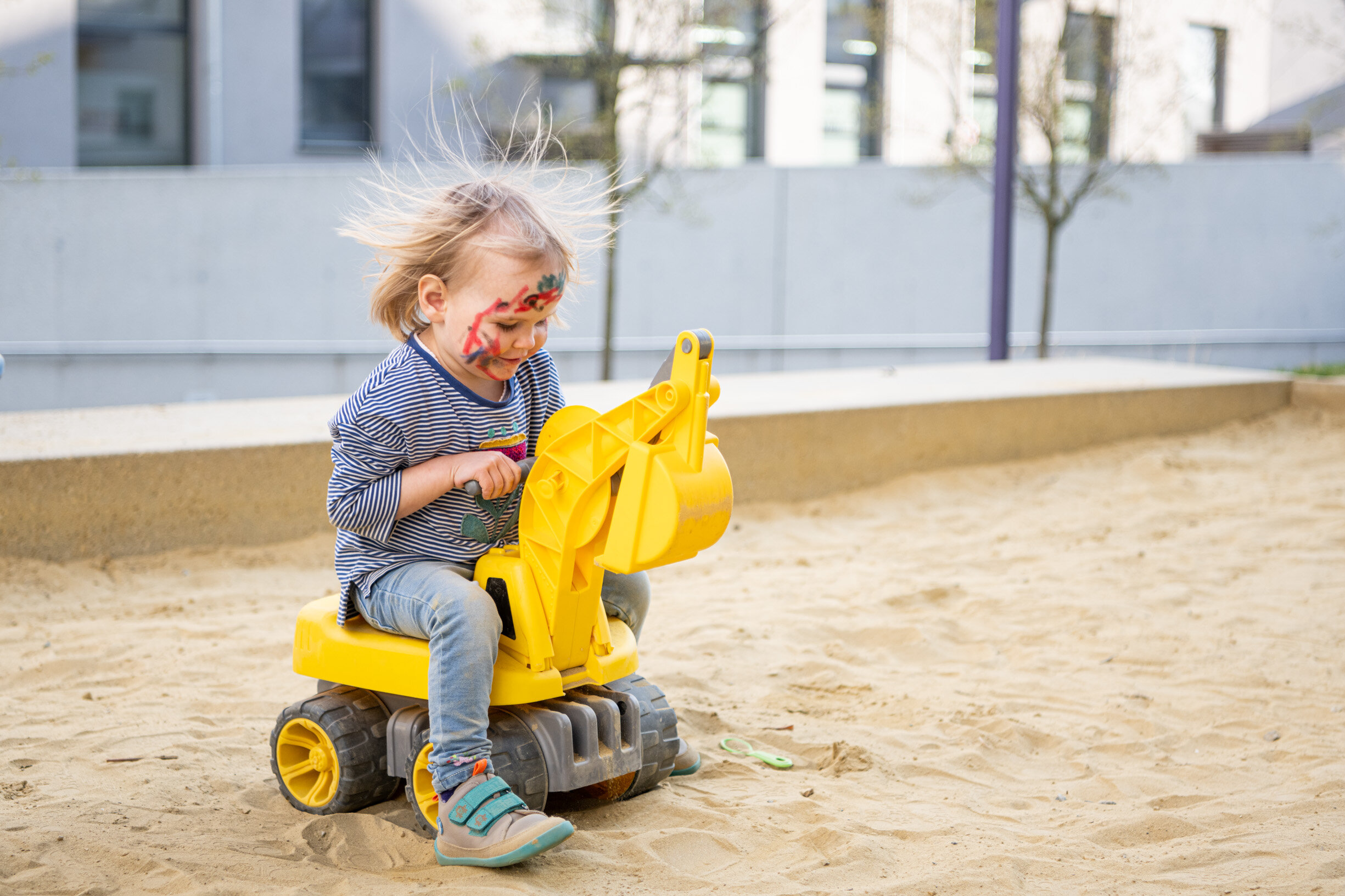 Mädchen spielt in Sandkiste mit Bagger