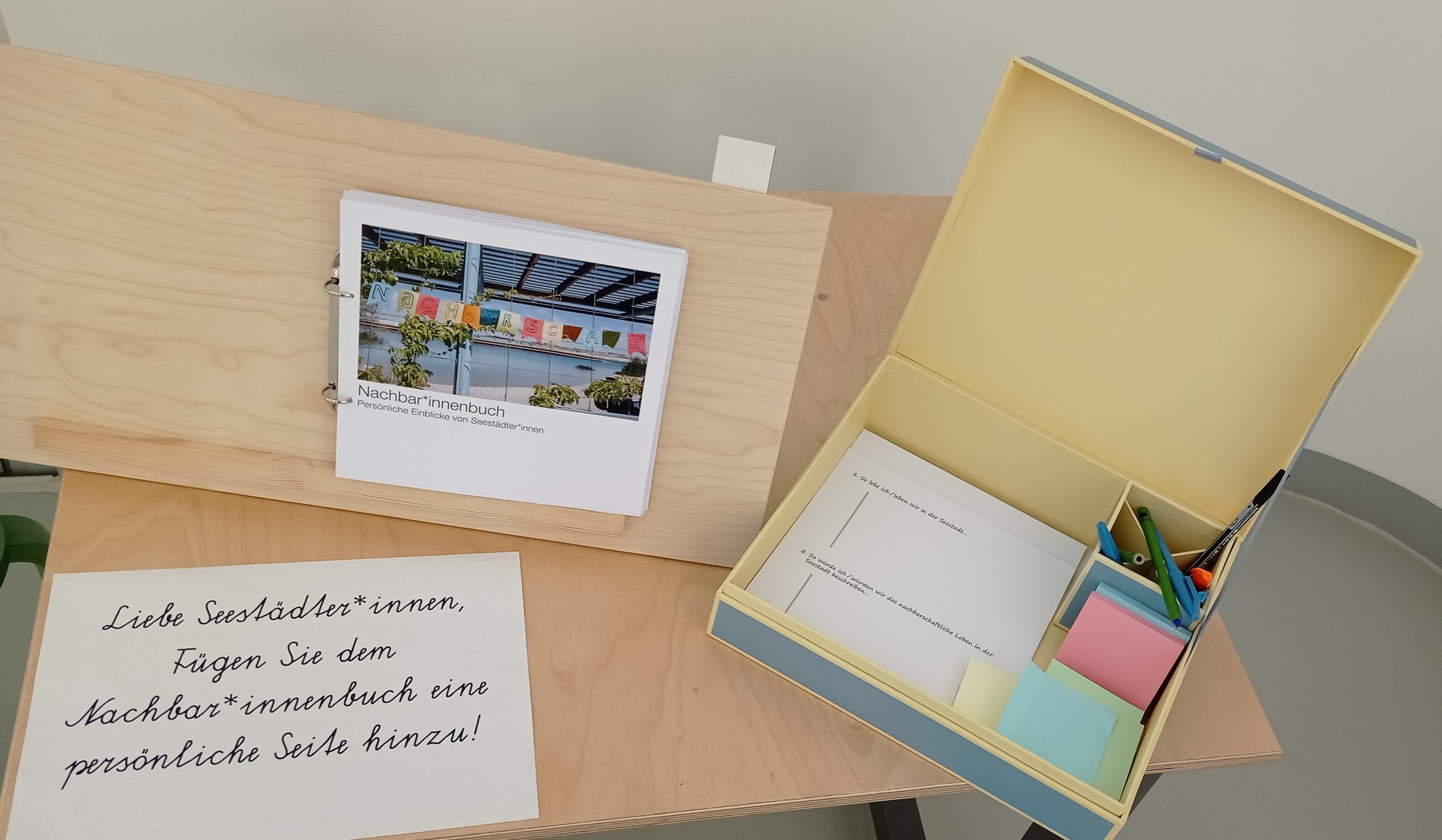 Ein Tisch auf dem das Nachbar*innenbuch des Stadtteilmanagements zu sehen ist und eine Bastelbox.