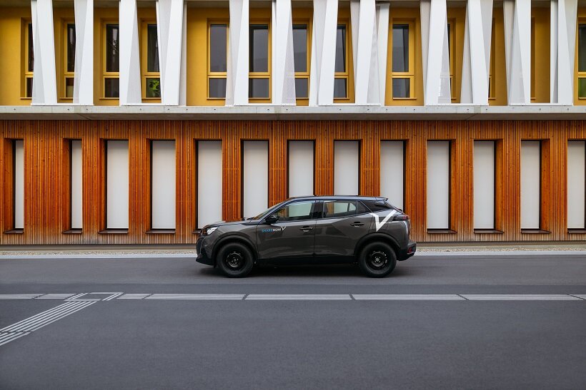 Ein Auto von Share now vor einer Holzfasade.