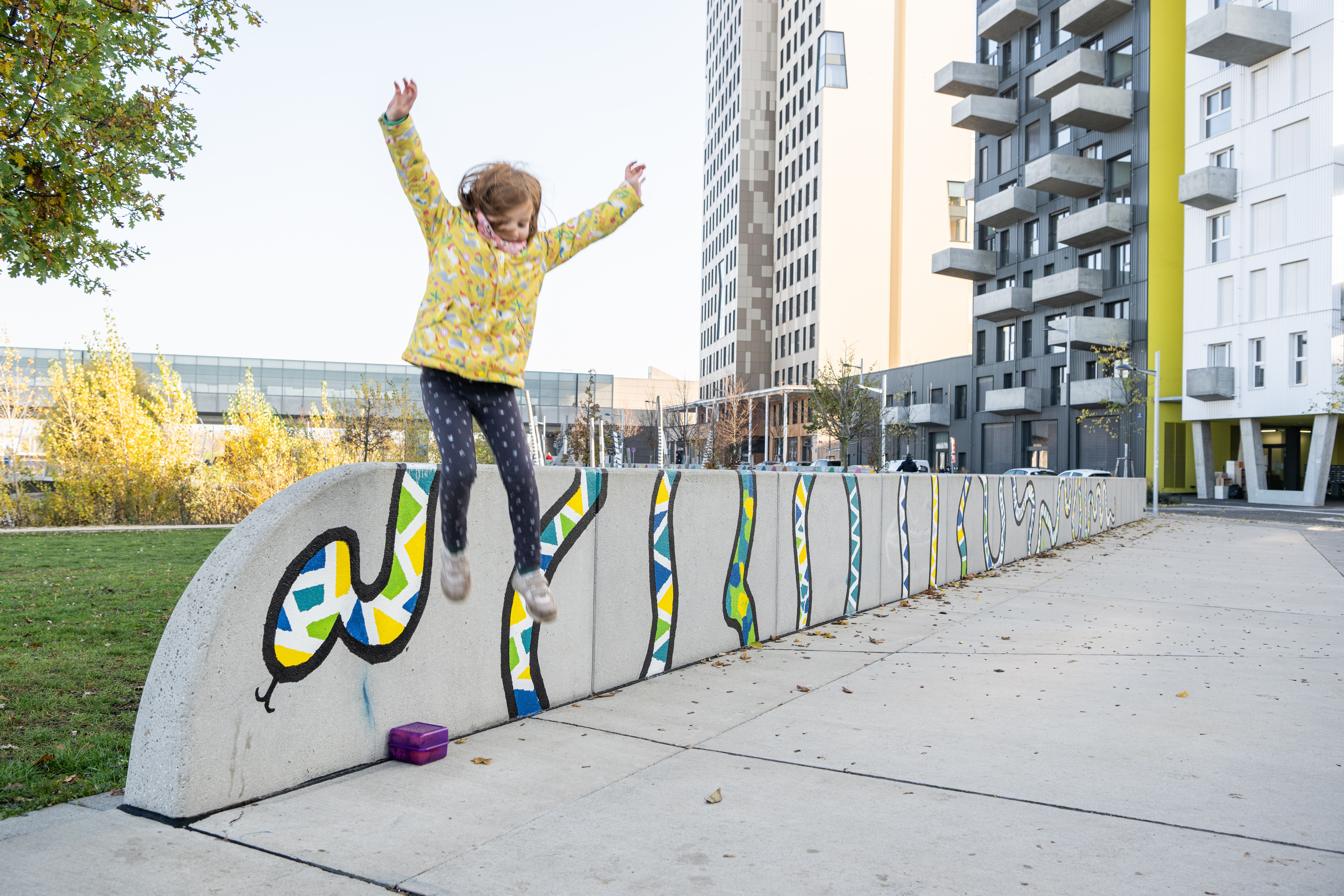 ein Kind springt spielerisch von einer niedrigen Mauer