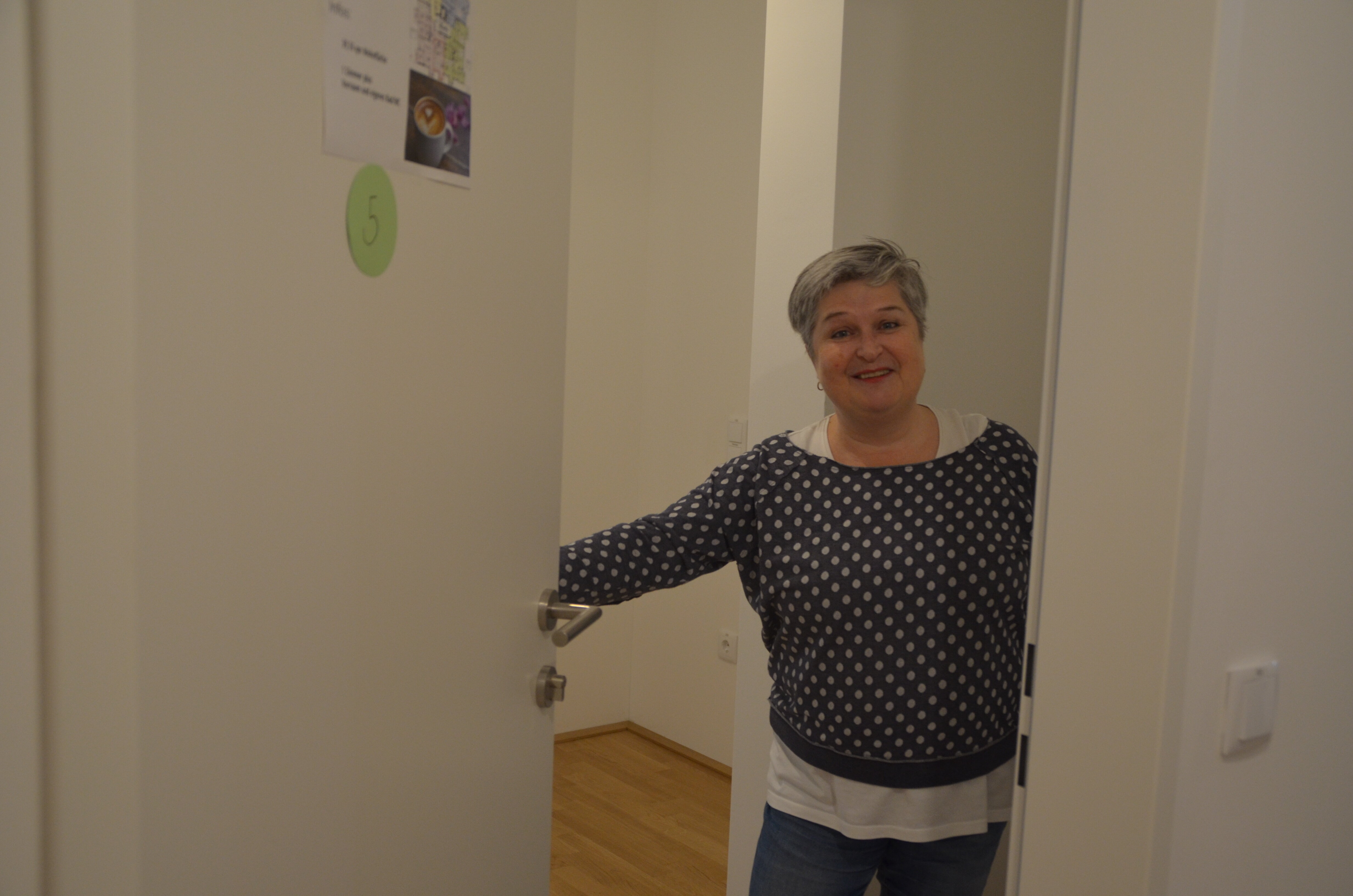 Eine Frau steht in der geöffneten Tür ihrer Wohnung und lacht.