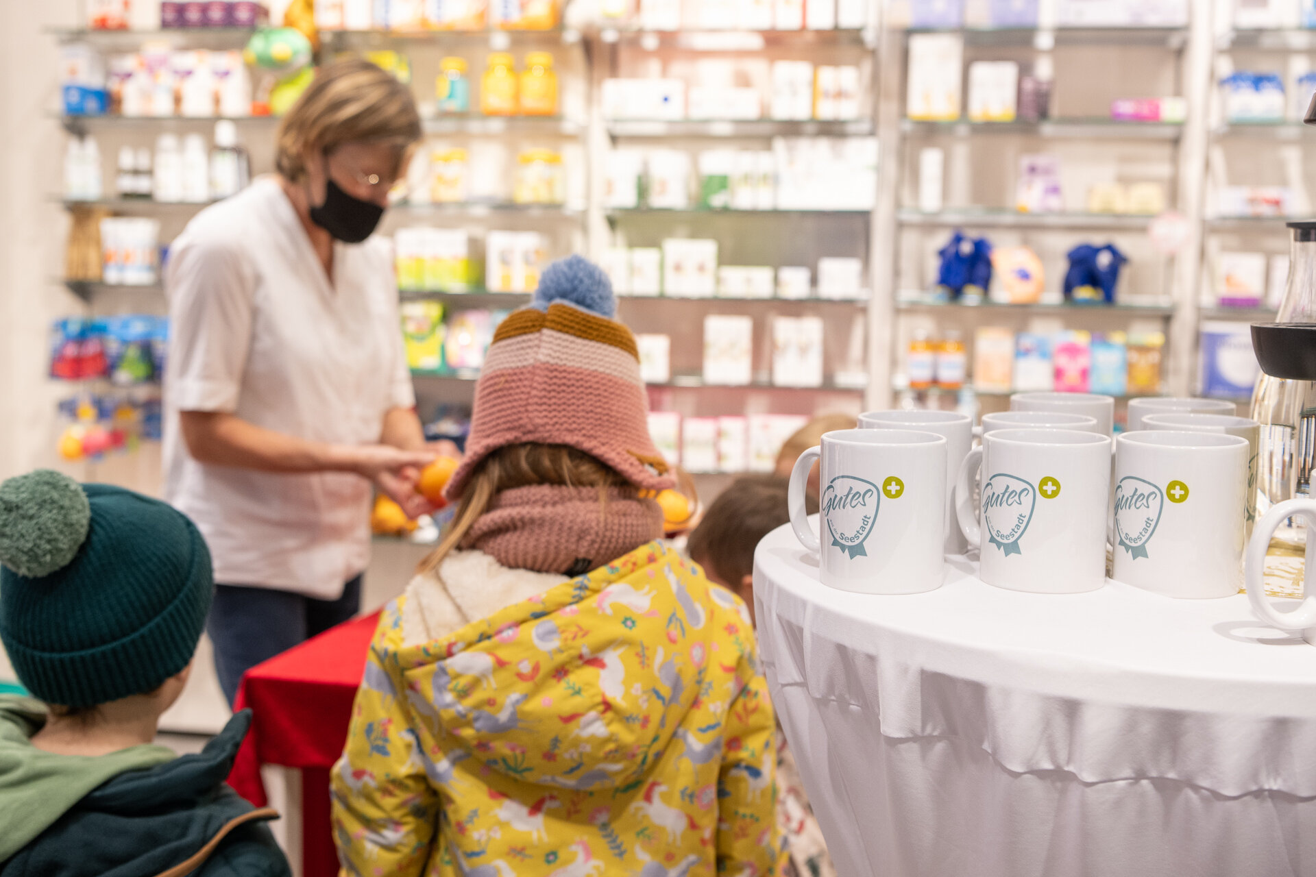 Apothekenmitarbeiterin empfängt Kinder, die den Seestadt Adventkalender besuchen, und gibt Orangen aus.