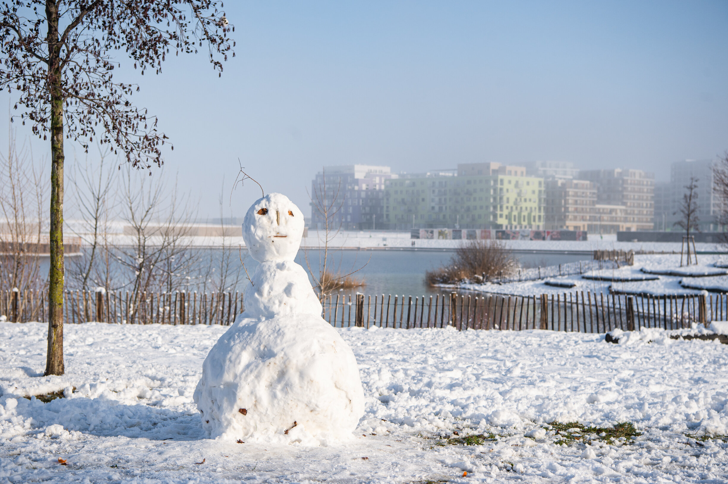Blick Richtung See. Im Vordergrund steht ein Schneemann.