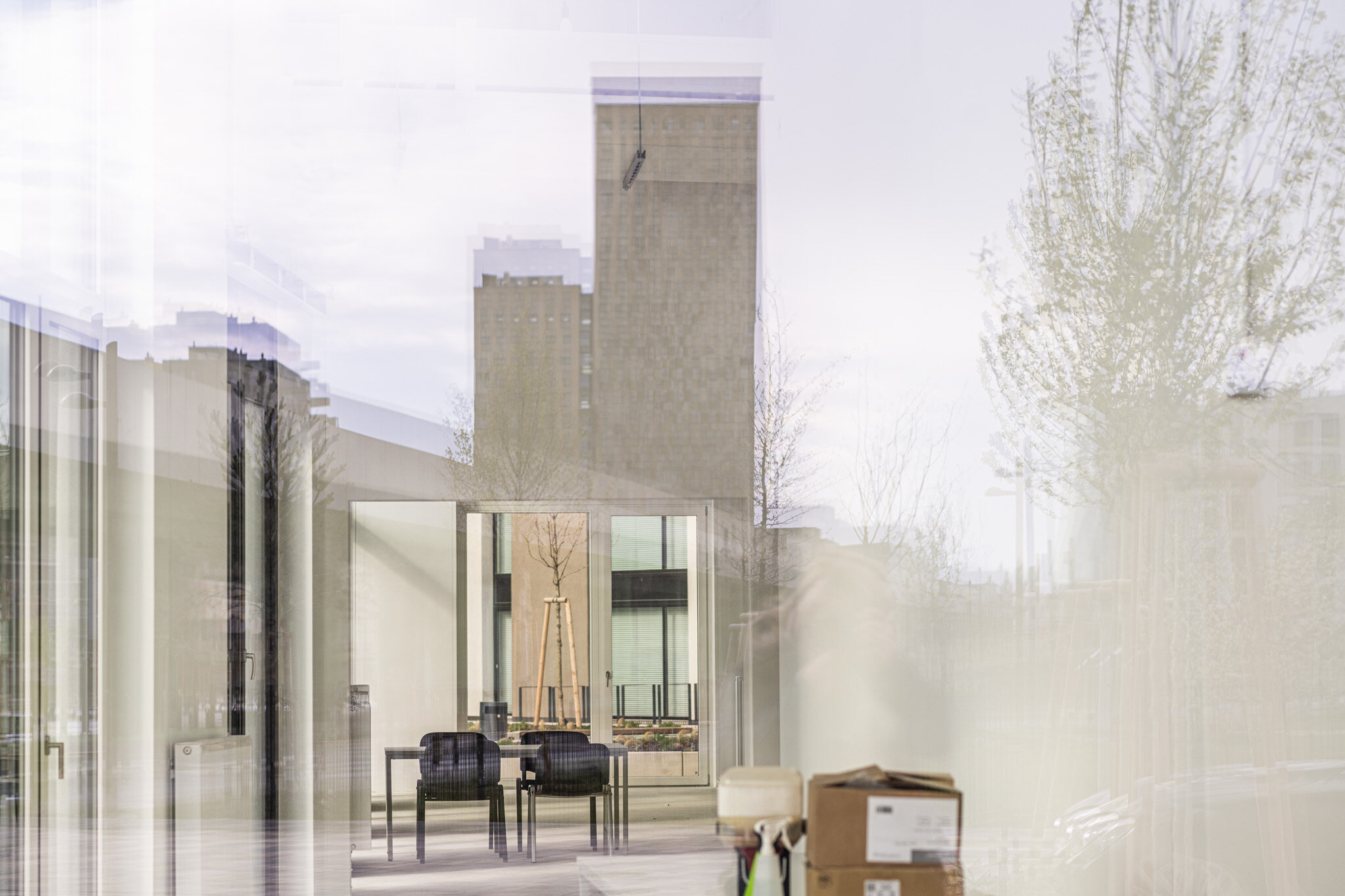 Blick durch eine Glasfassade in einen Innenraum eines Gebäudes. zu sehen ist ein Tisch mit Sesseln.