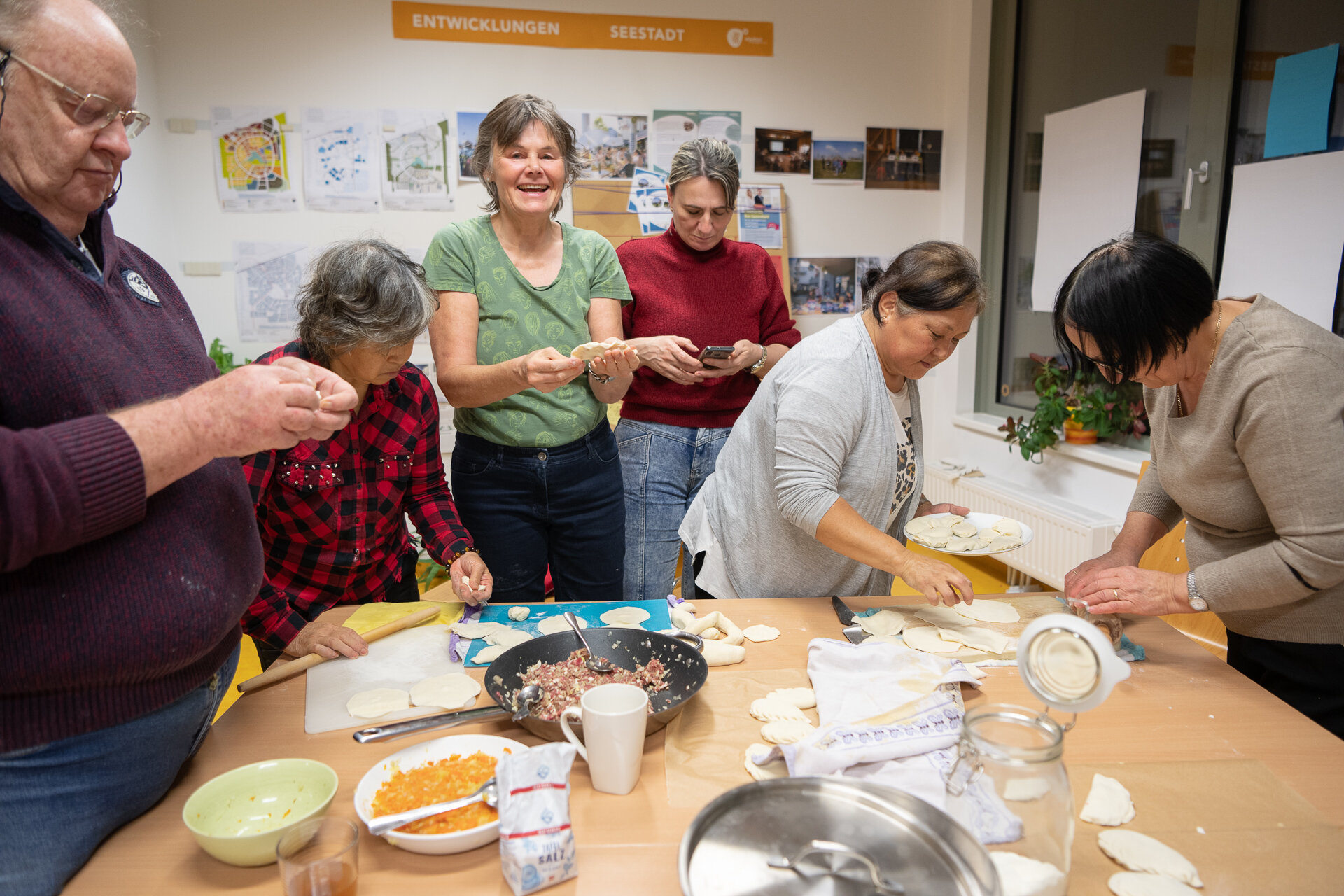 Nachbar*innen stehen im Stadtteilmanagement um einen Tisch und bereiten gemeinsam eine Speise vor.