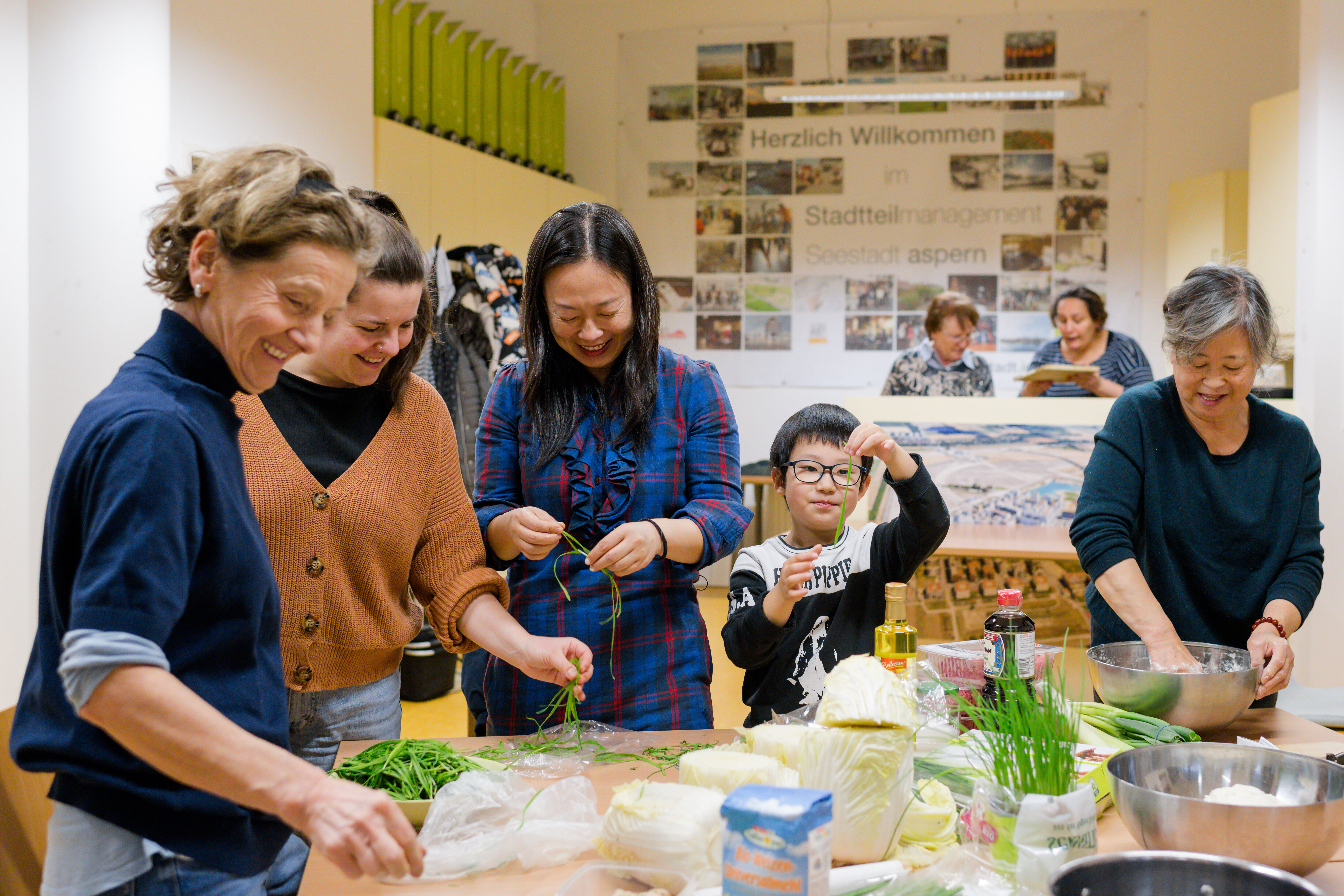 Mehrere Menschen stehen um einen Tisch und bereiten die Zutaten für Teigtaschen vor.
