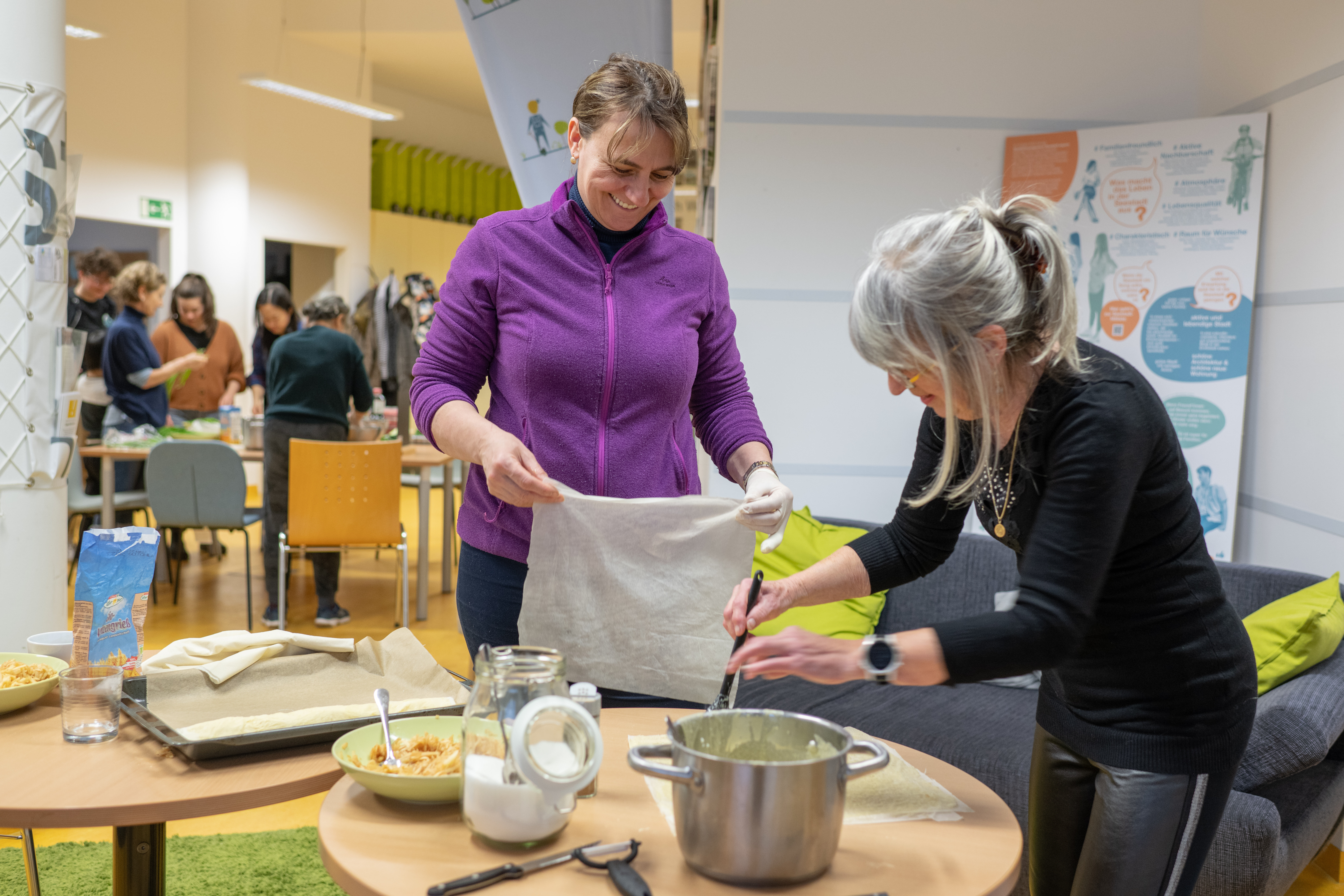 Zwei Frauen stehen an einem Tisch und bereiten Apfelstrudel zu. 