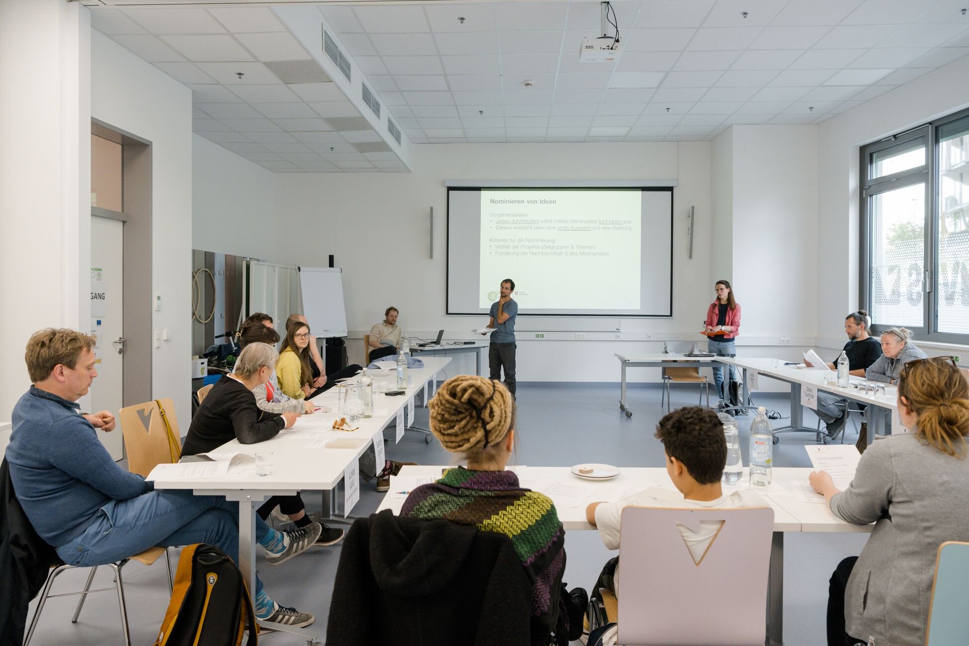 Menschen sitzen an Tischen un U-Form und beraten sich