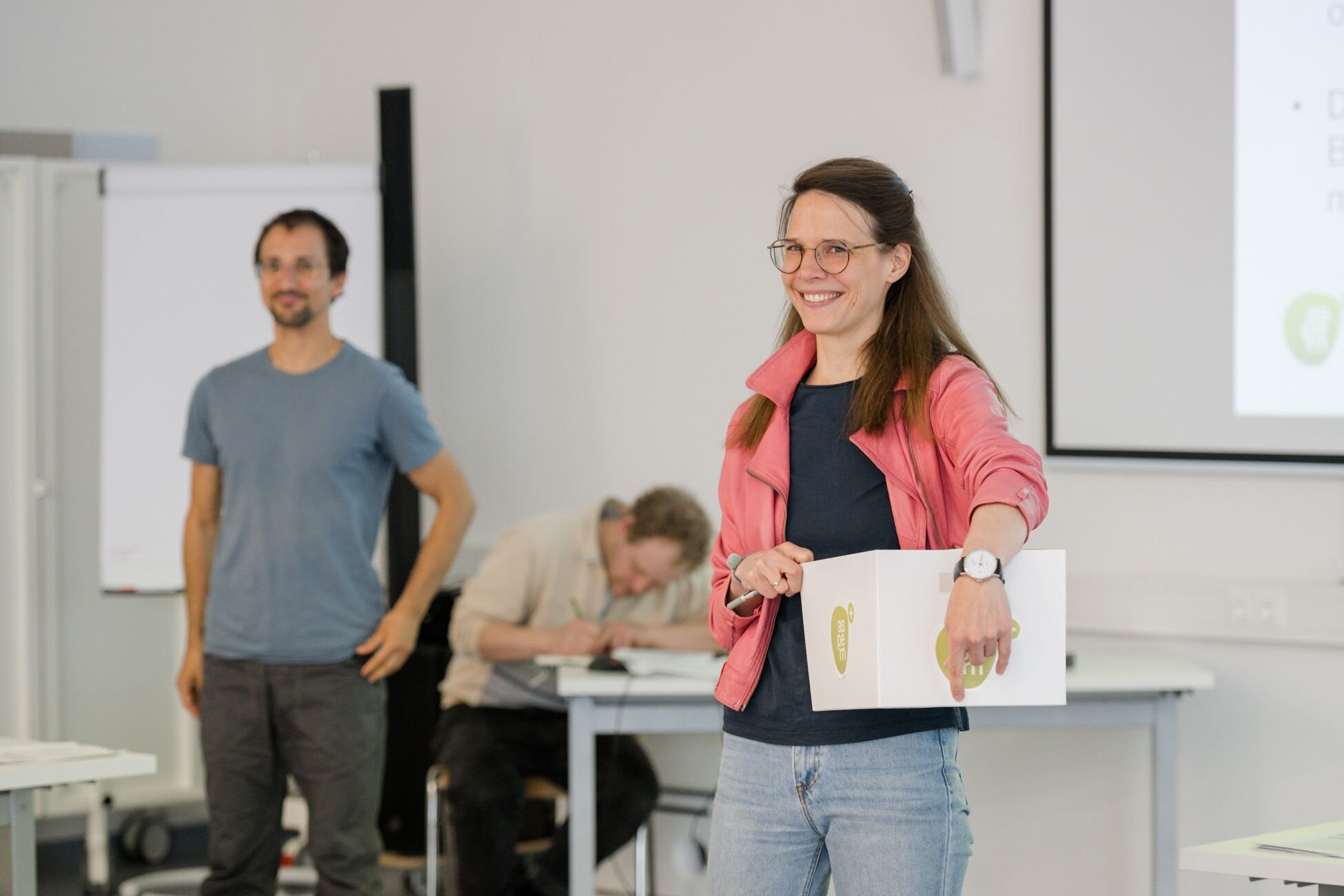 Zwei Menschen im Bild. Eine Person hält eine weiße Box in der Hand