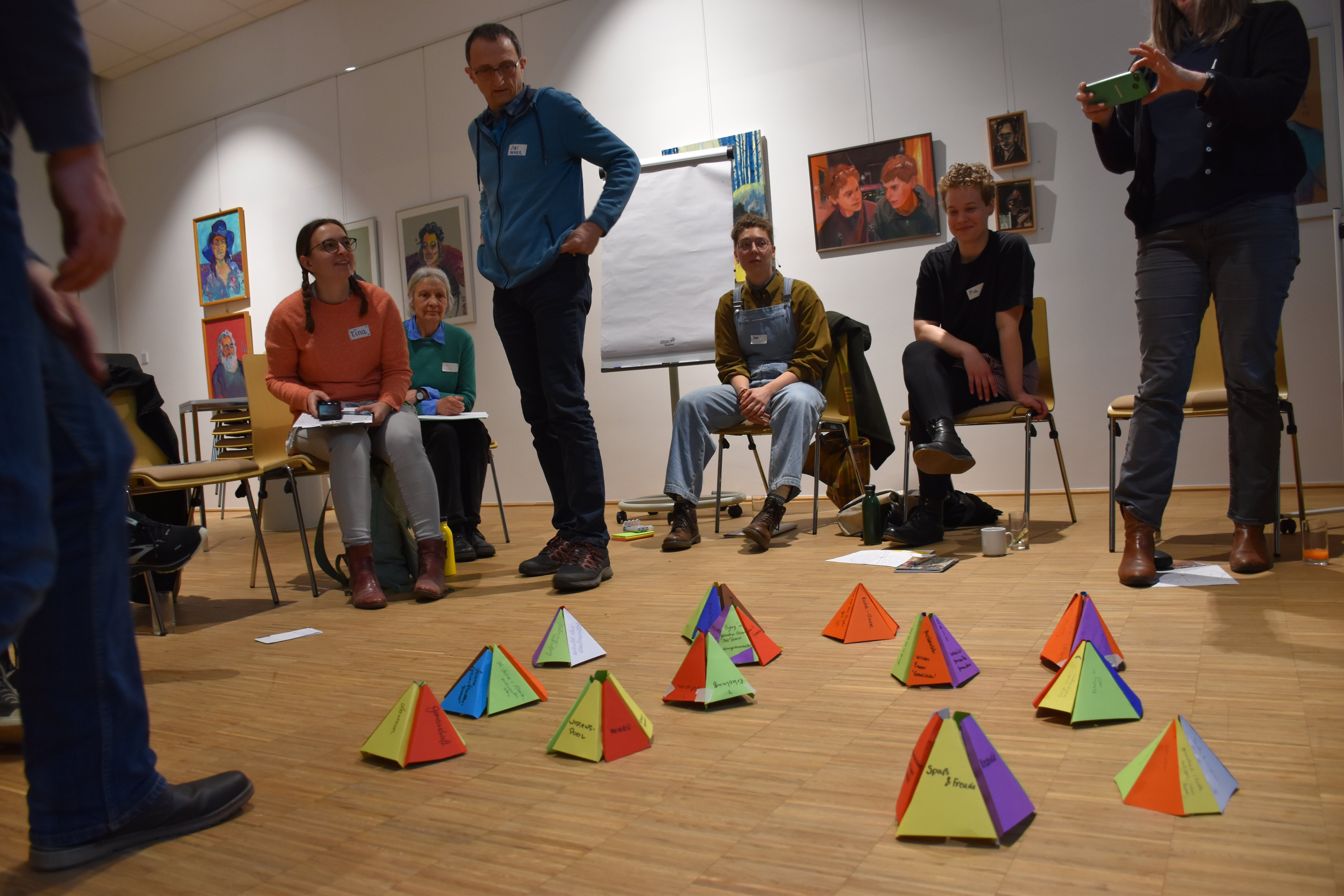 kleine Pyramiden aus Papier stehen am Boden. Menschen stehen im Hintergrund