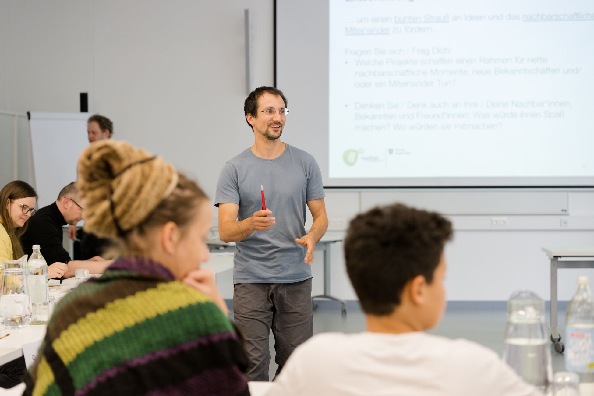 ein Mann steht in der Mitte des Bildes. Im Vordergrund sind zwei Menschen von Hinten sichtbar