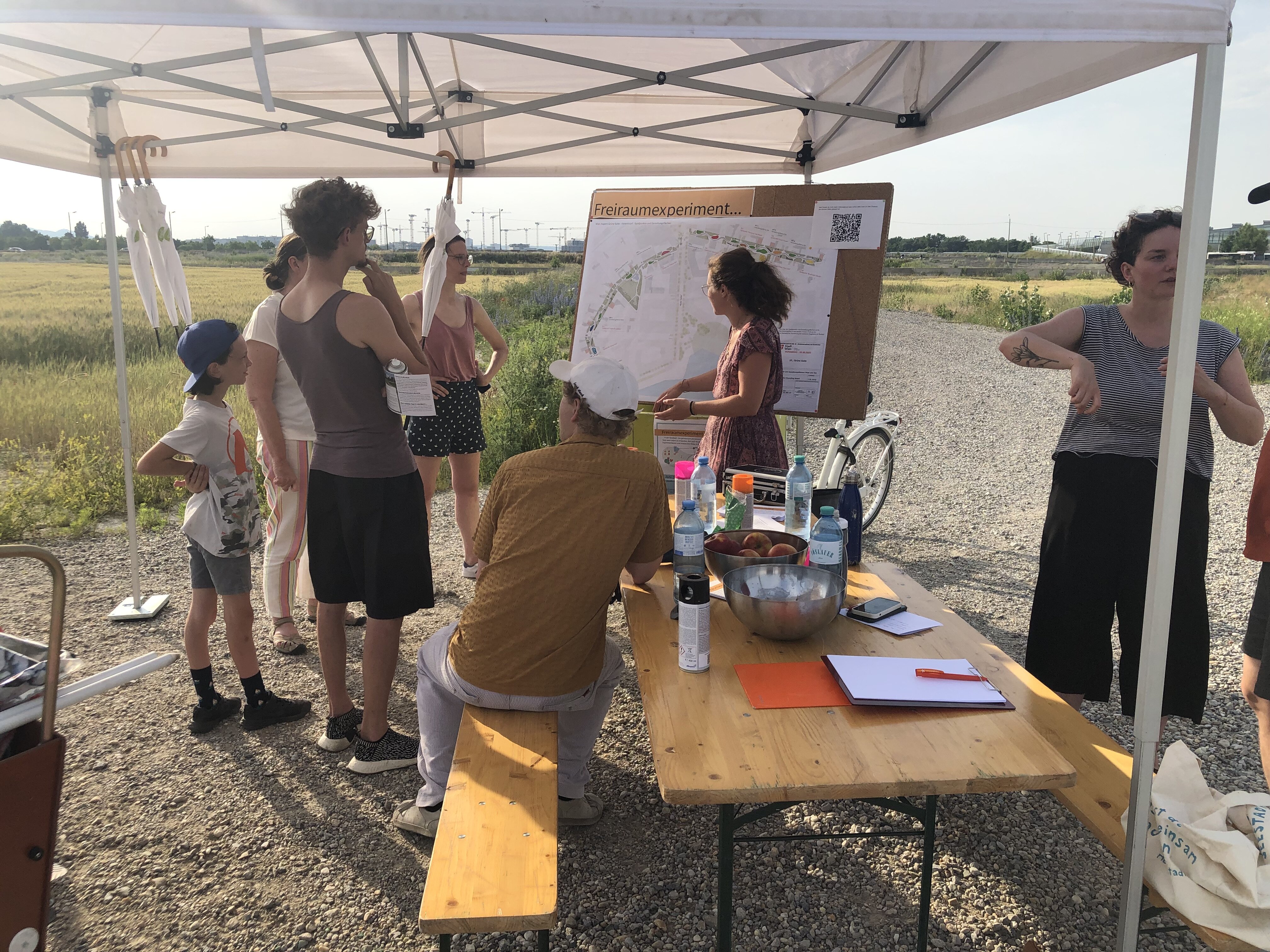 Menschen sitzen an Biertisch und diskutieren über einen Plan auf einem Ständer