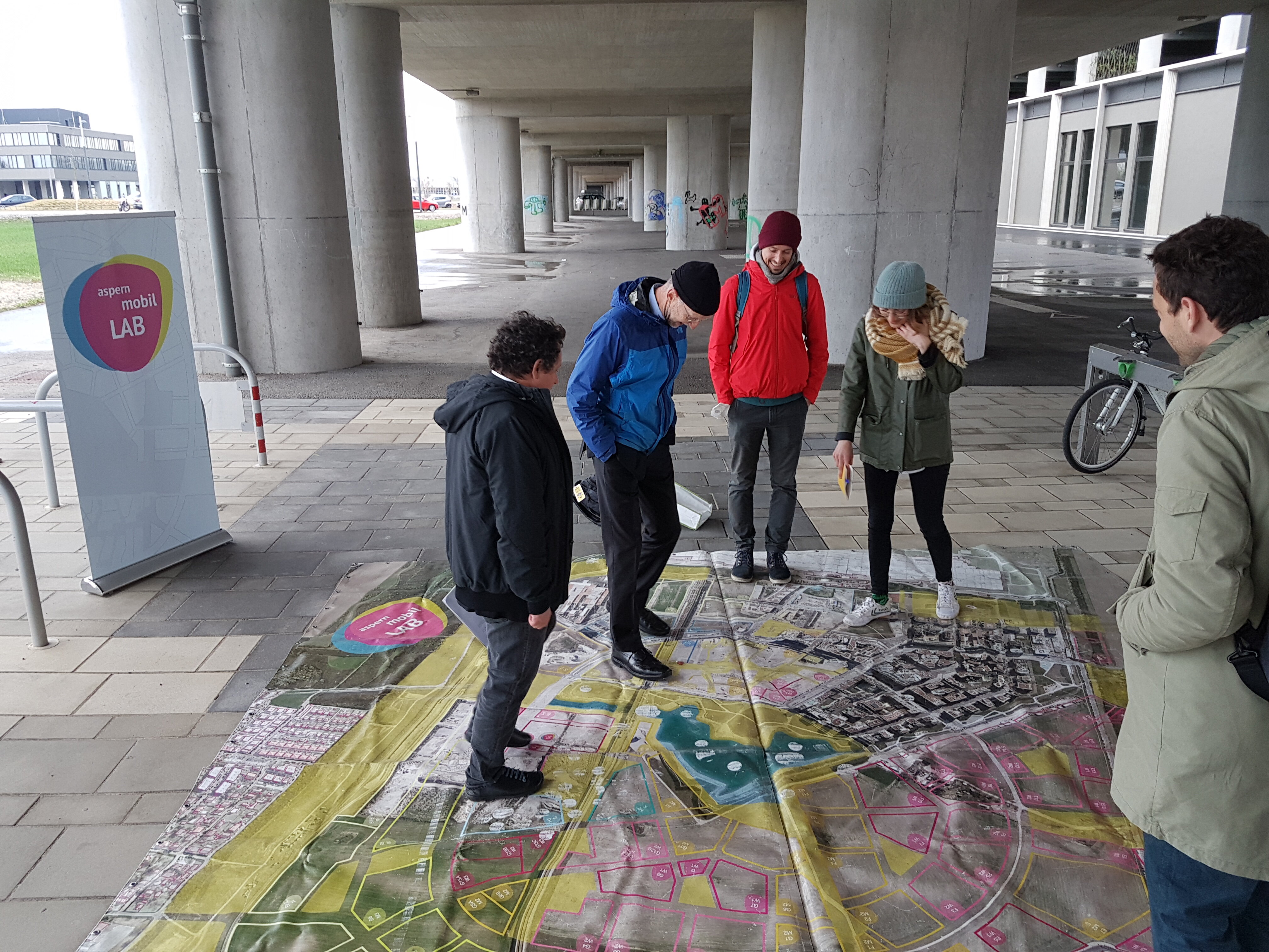 Menschen stehen unter der Ubahnbrücke auf einem Plan des AML