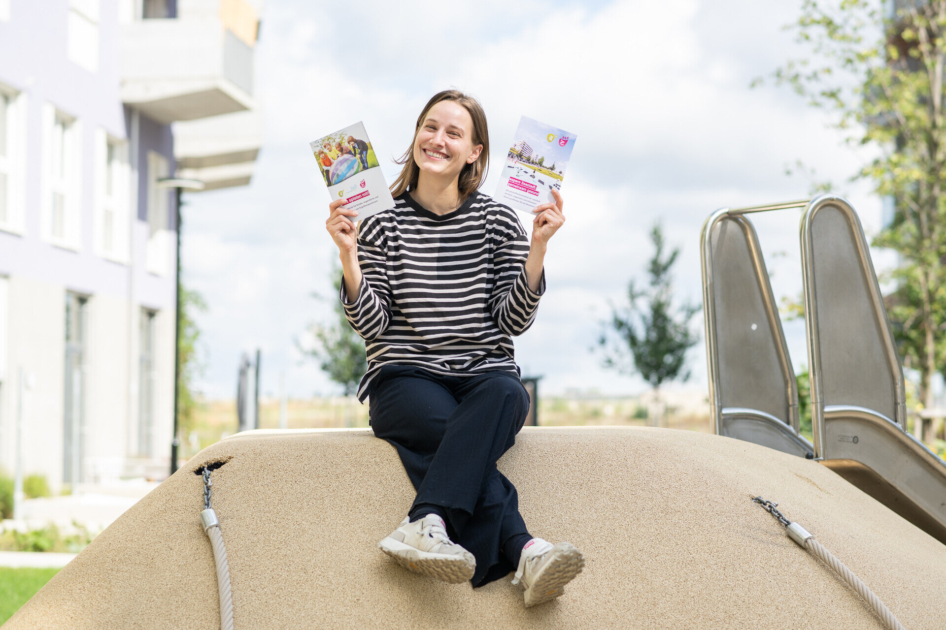 eine Frau sitzt am Spielplatz und hält Flyer in der Hand