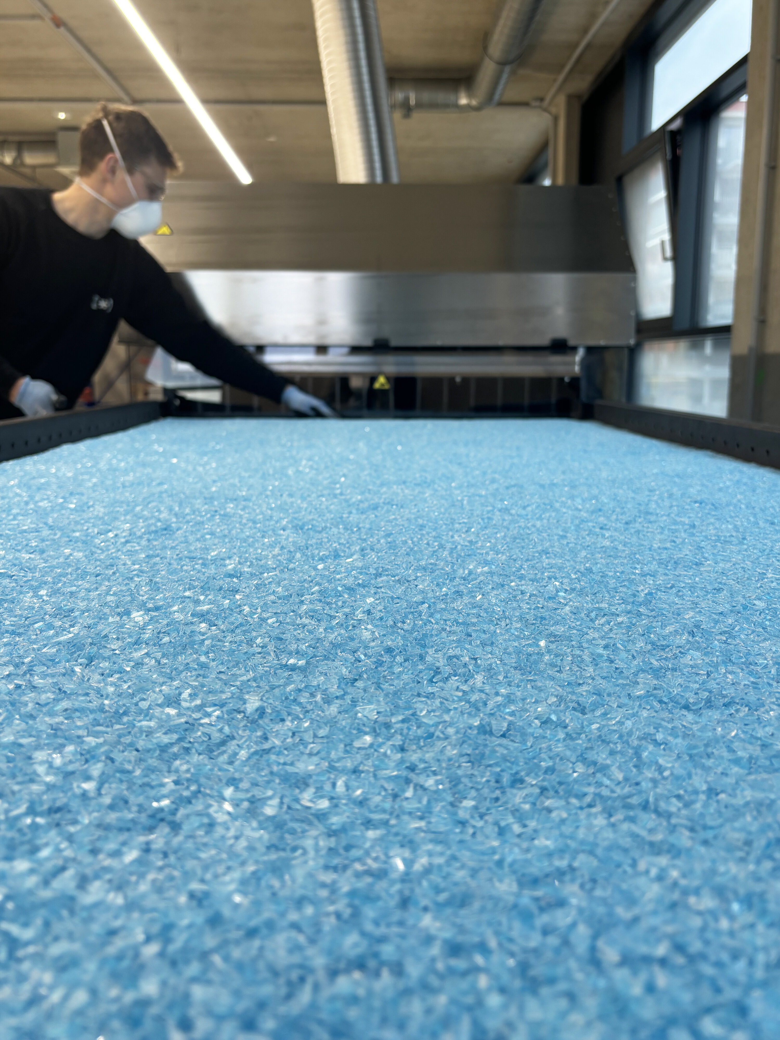 Kunststoffgranulat auf einem Förderband mit einem Mitarbeiter.